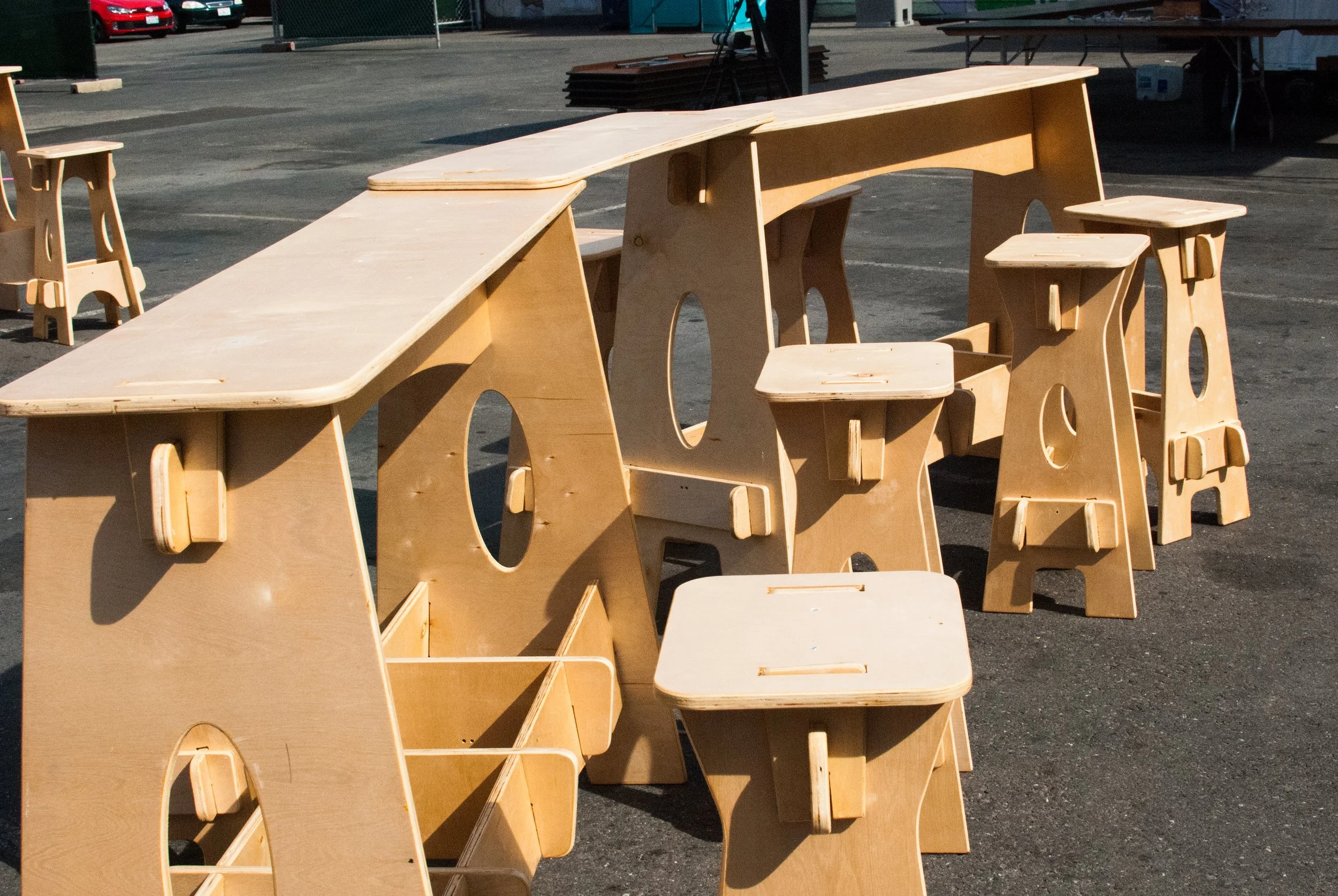 Unfinished wooden school desks and chairs stacked outdoors in a parking lot