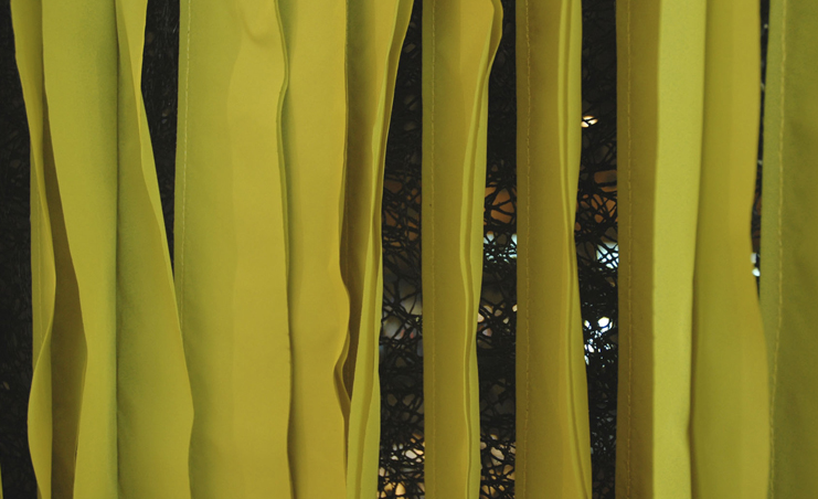 Close-up of vertical yellow ribbon strips hanging with a dark patterned background visible through gaps.