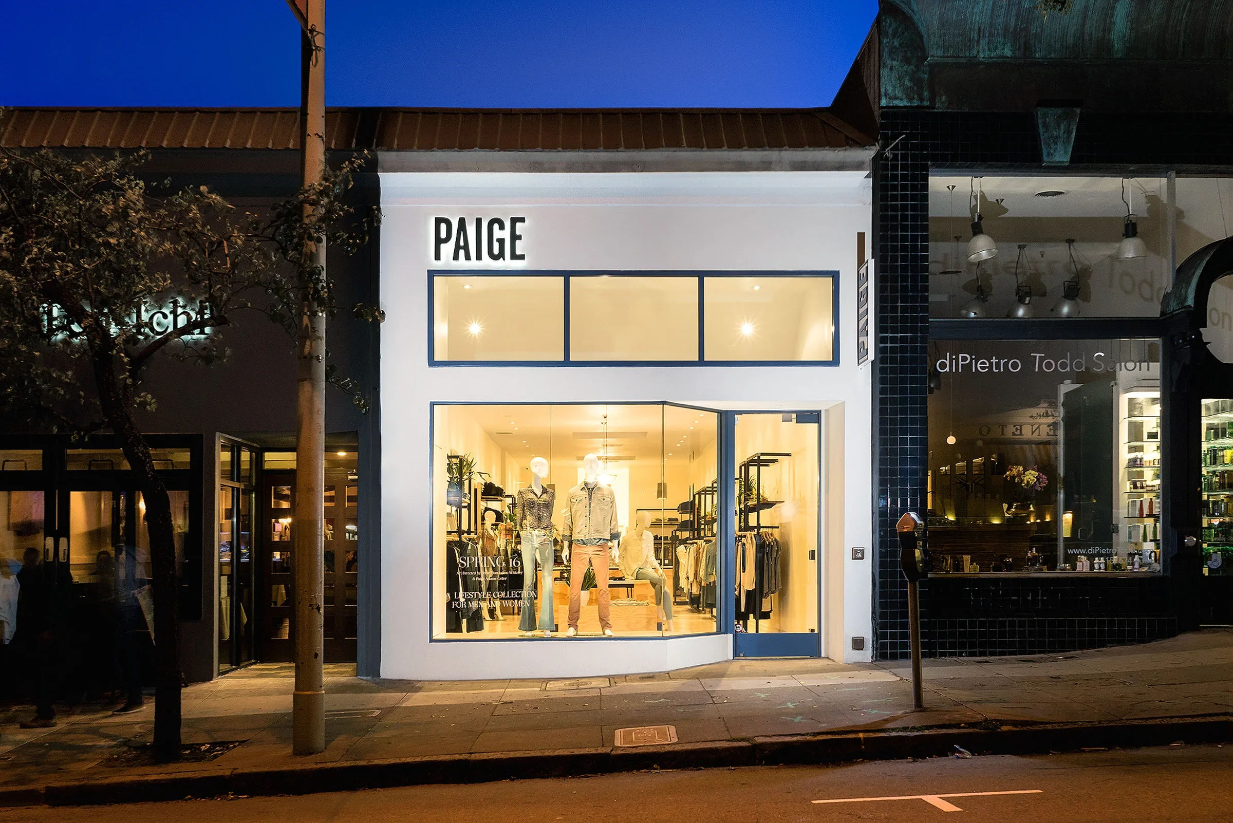 Storefront of paige denim in the evening. The storefront is primarly windows, with a set of high clerestory windows below the store signage.