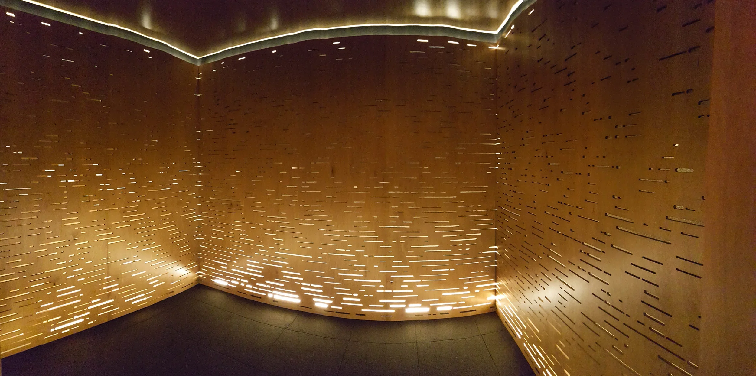 Interior of the meditation room, where a series of vertical cavities are cut out of plywood walls and are illuminated by LED light coming from the ground.