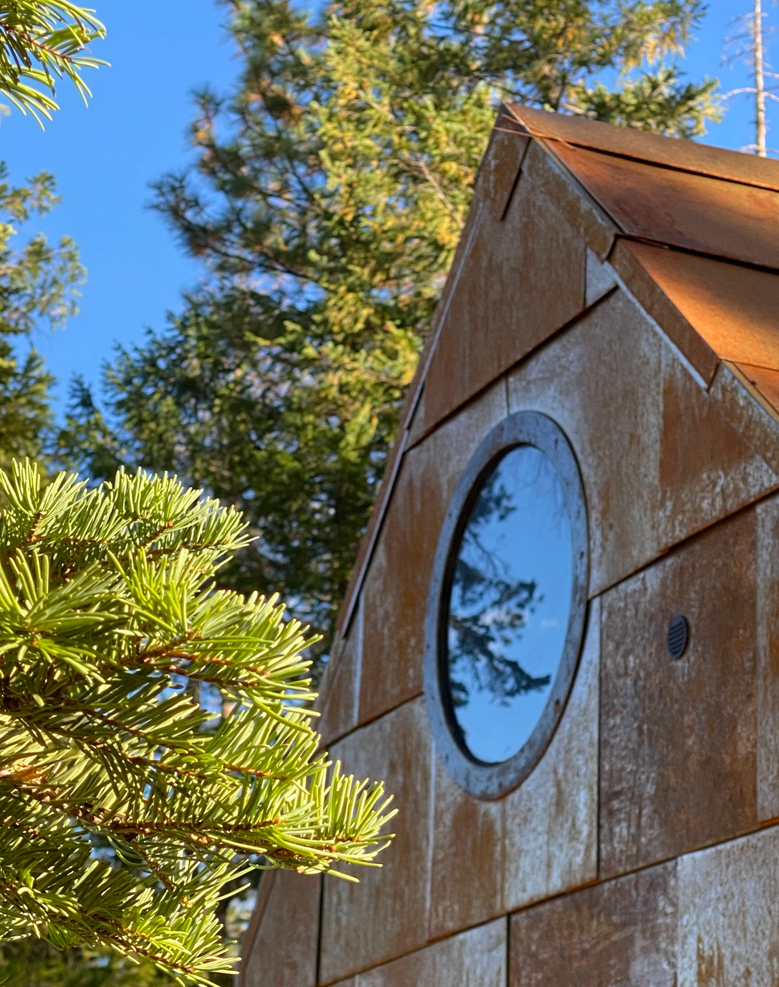 The steel, weathered by the seasons, stands out against an evergreen forest of pine trees.