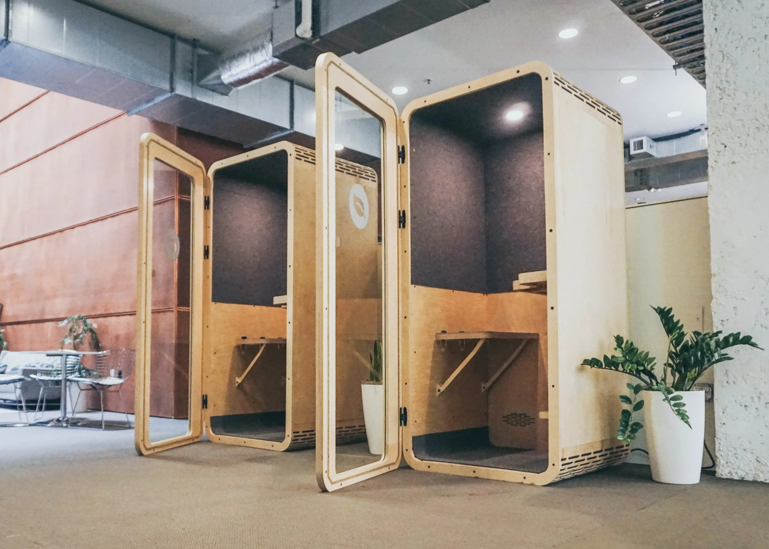 Two jumpbooths installed. Their wooden structure has a solid plexi-glass door. The inside of the booths is finished with gray, textured acoustic insulation and wood plywood paneling.