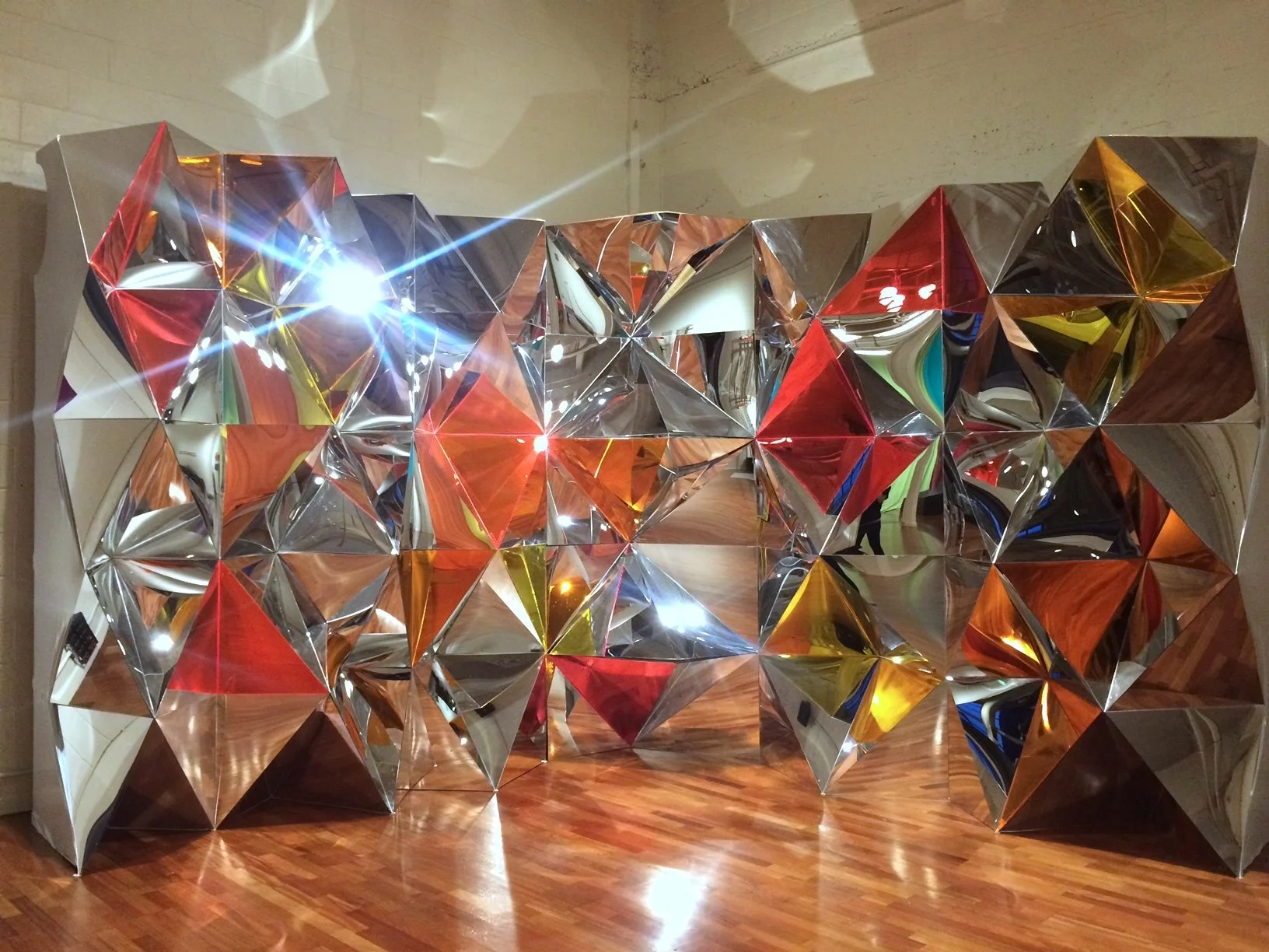 A contemporary art installation, made from geometric shapes, clad in mirror-like or orange, red and yellow panels
