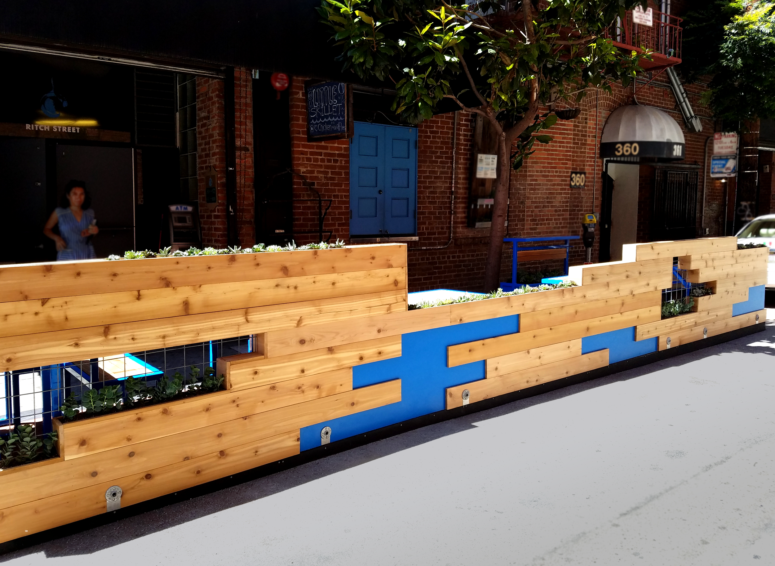 Parklet walls are made fom horizontal cedar planks. In some spots, a lack of panels reveal a cobalt blue section, or expose planters, giving the entire parkelt a pixelated feel.