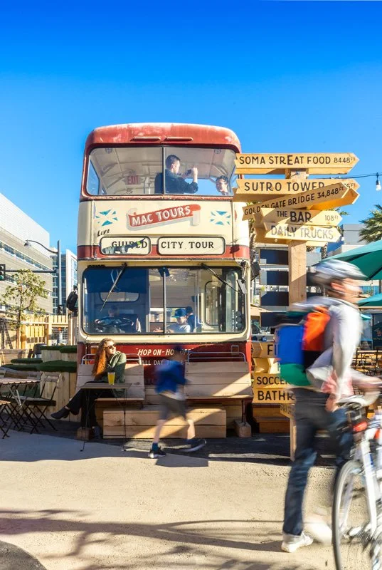 A converted double decker bus anchors the bustling food truck park, converting the interior into seating, and an instagrammable moment. Custom seating and signage made from cedar add a neighborly, outdoorsy feel.
