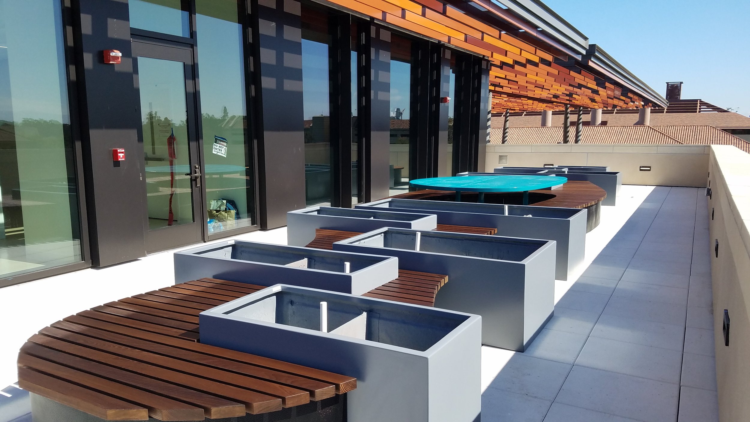 Mid-Install: Organic-shapped cedar bench weaves through gray metal planters on Stanford's Bass Biology Research Building's rooftop terrace.