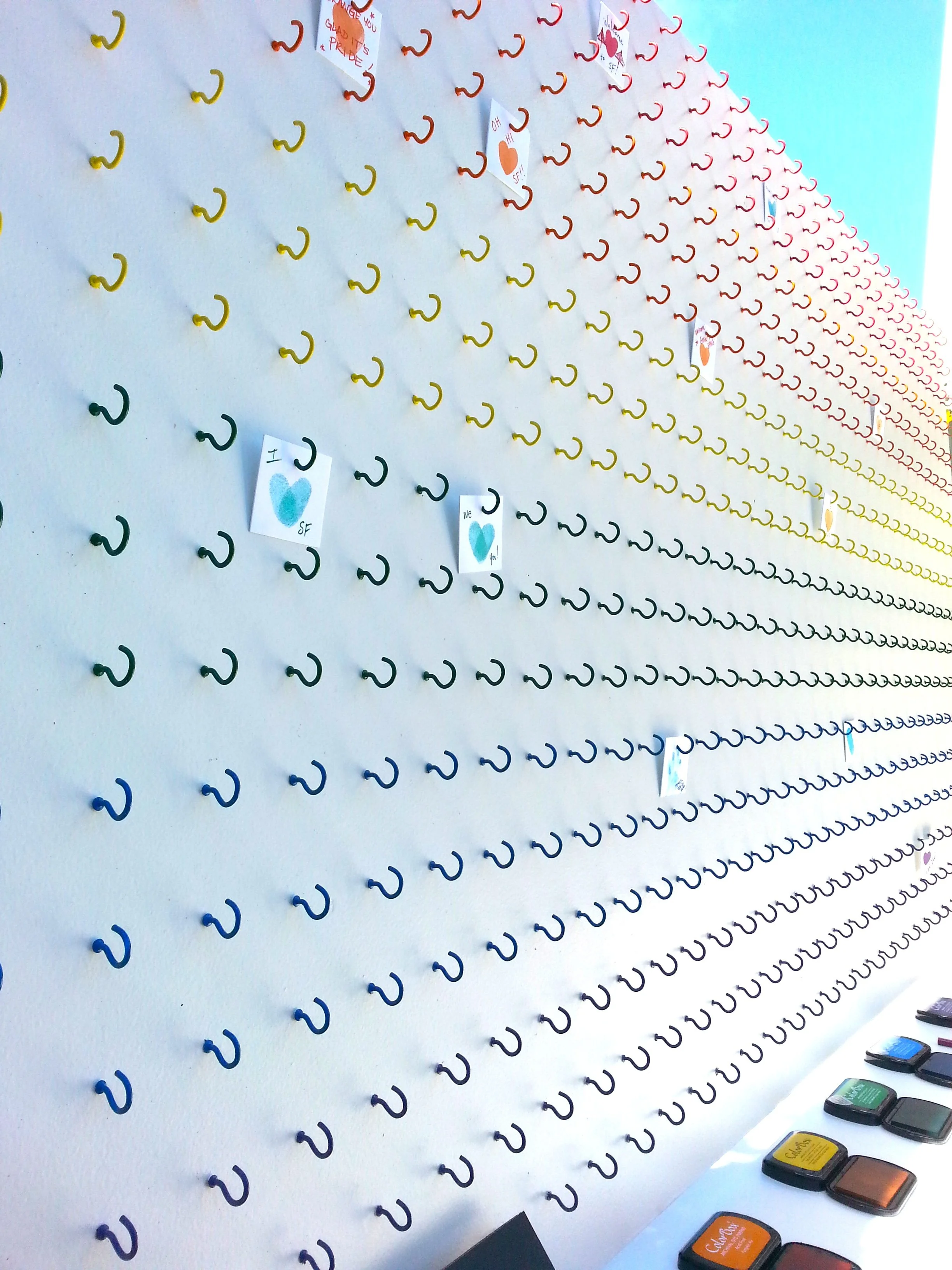 An interactive board, made up of hooks in the color of the rainbow, invites folks to create and hang their own stamped artwork.