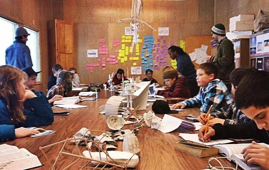 Particioants brainstorm ideas around a large table, looking over books and writing notes. Interpretive models are a tool to align ideas.