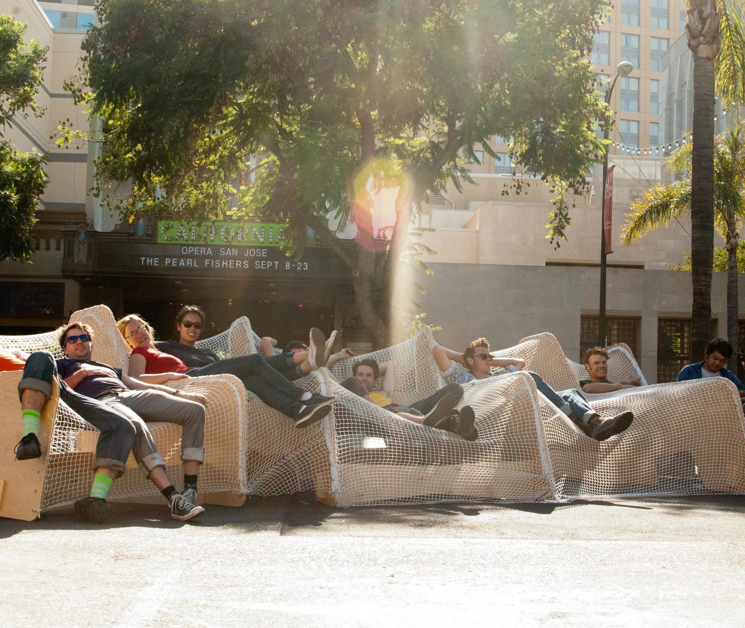 Folks lounge in a temporary seating installation, made from a netting material drapped over plywood, chair-like forms.
