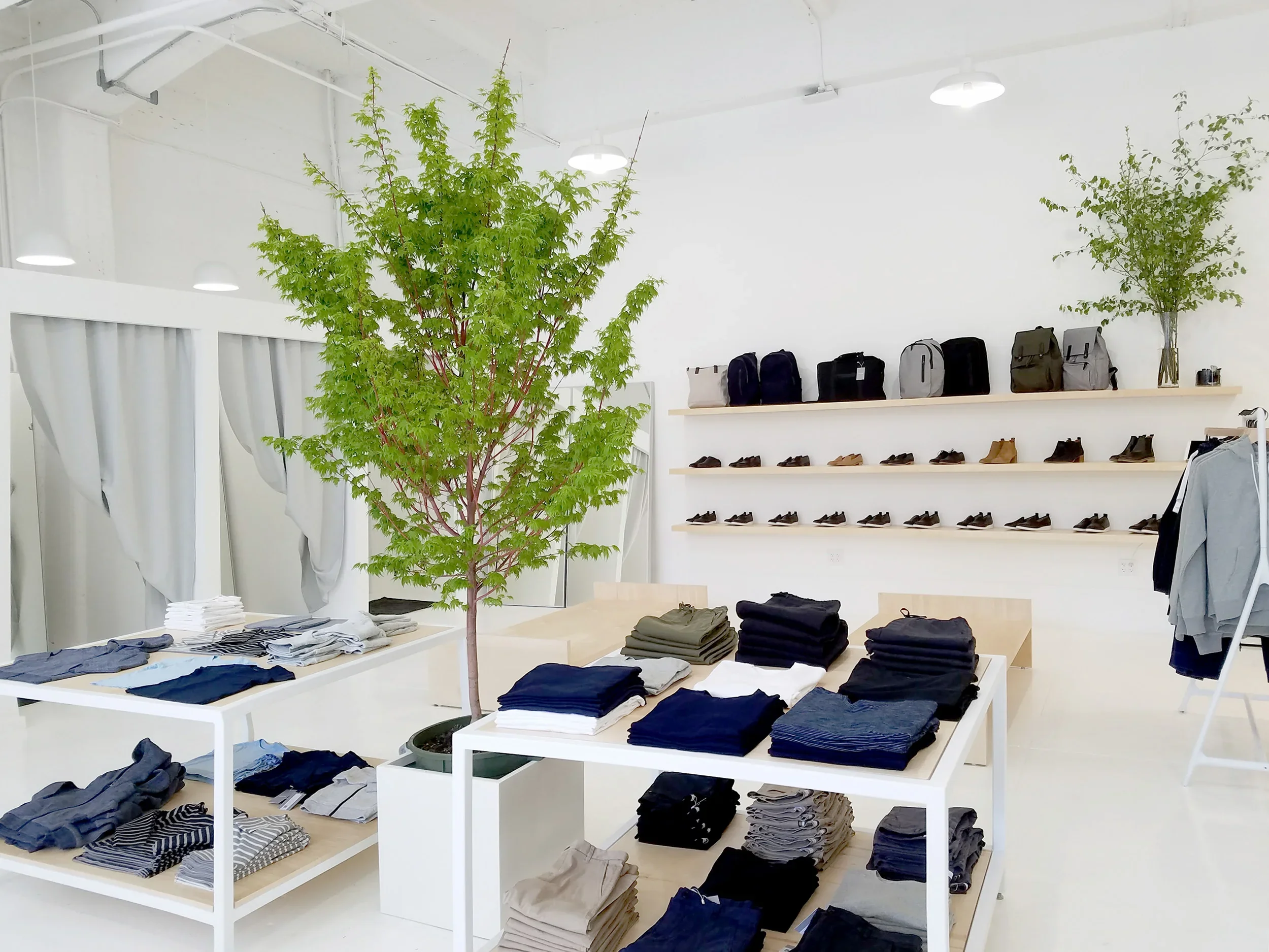 Custom-fabricated retail displays are nestled between small trees. In the background are changing rooms.