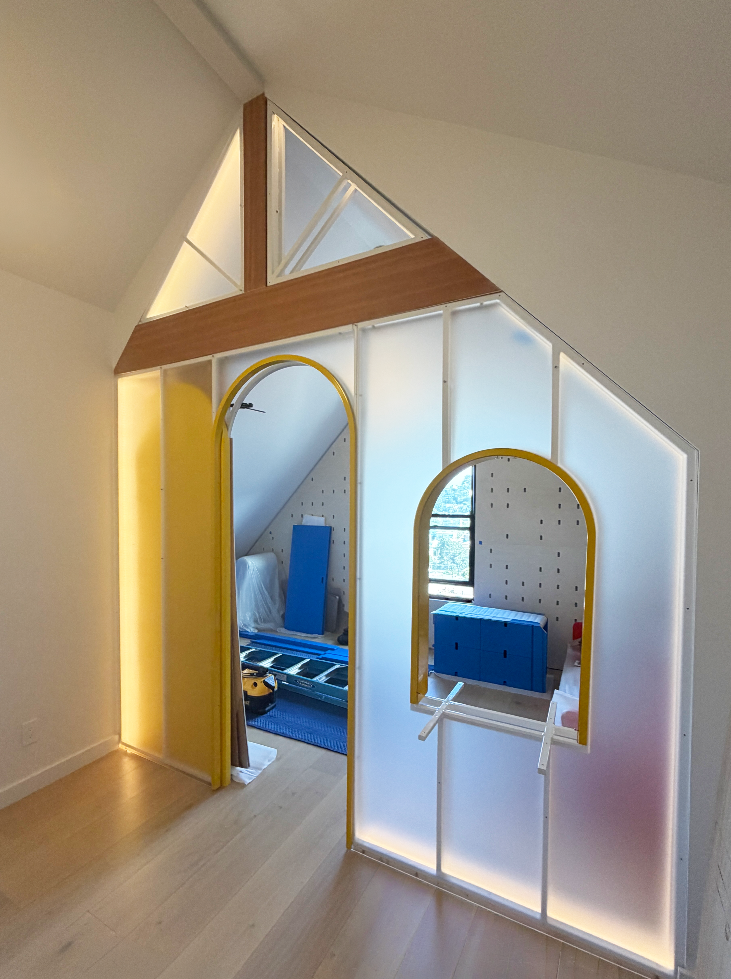 Interior of a room under construction with a partially assembled structure, yellow trim, circular mirrors, and construction tools.