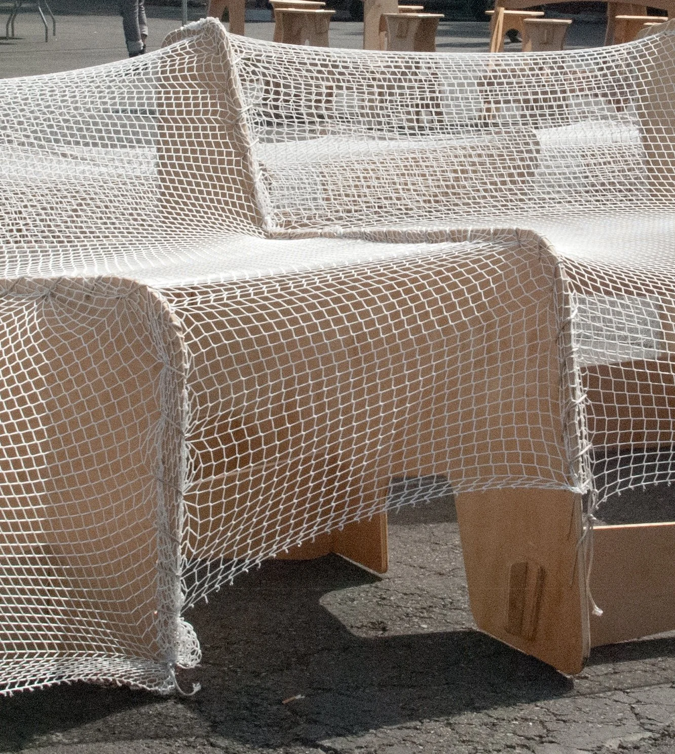 Close-up of an interactive seating solution, where a fishing net-like mesh is draped over a series of plywood shapes, creating comfy, deep-seated chairs.