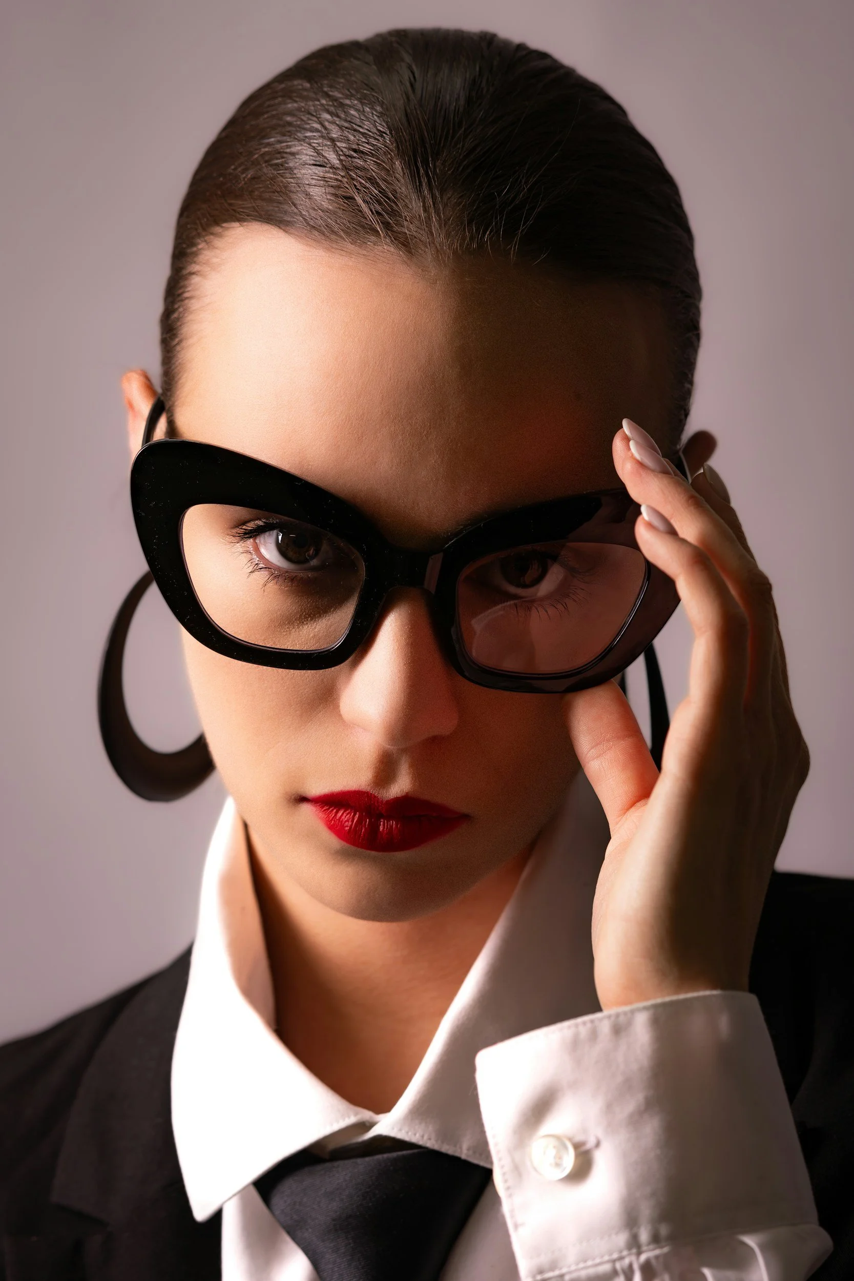 A woman with dark hair, red lipstick, and wearing sunglasses.