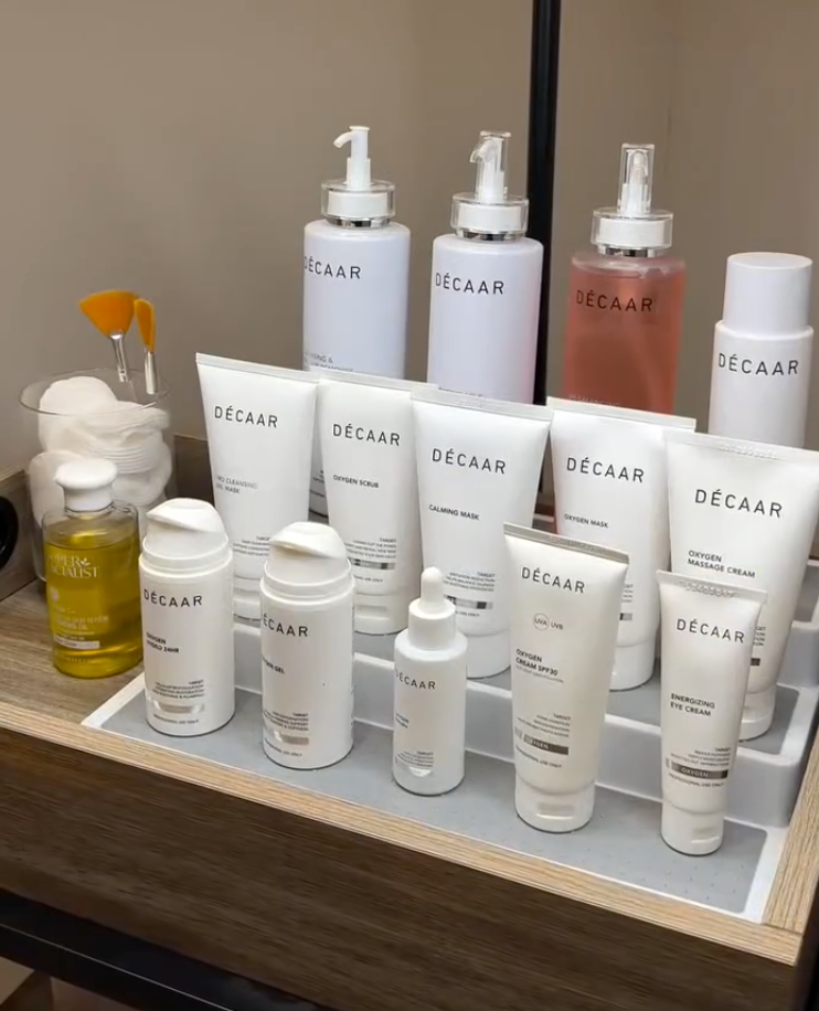 Skincare products on a wooden tray, including cleansers, masks, serums, and creams, labeled 'DÉCAAR' with a mirror behind.