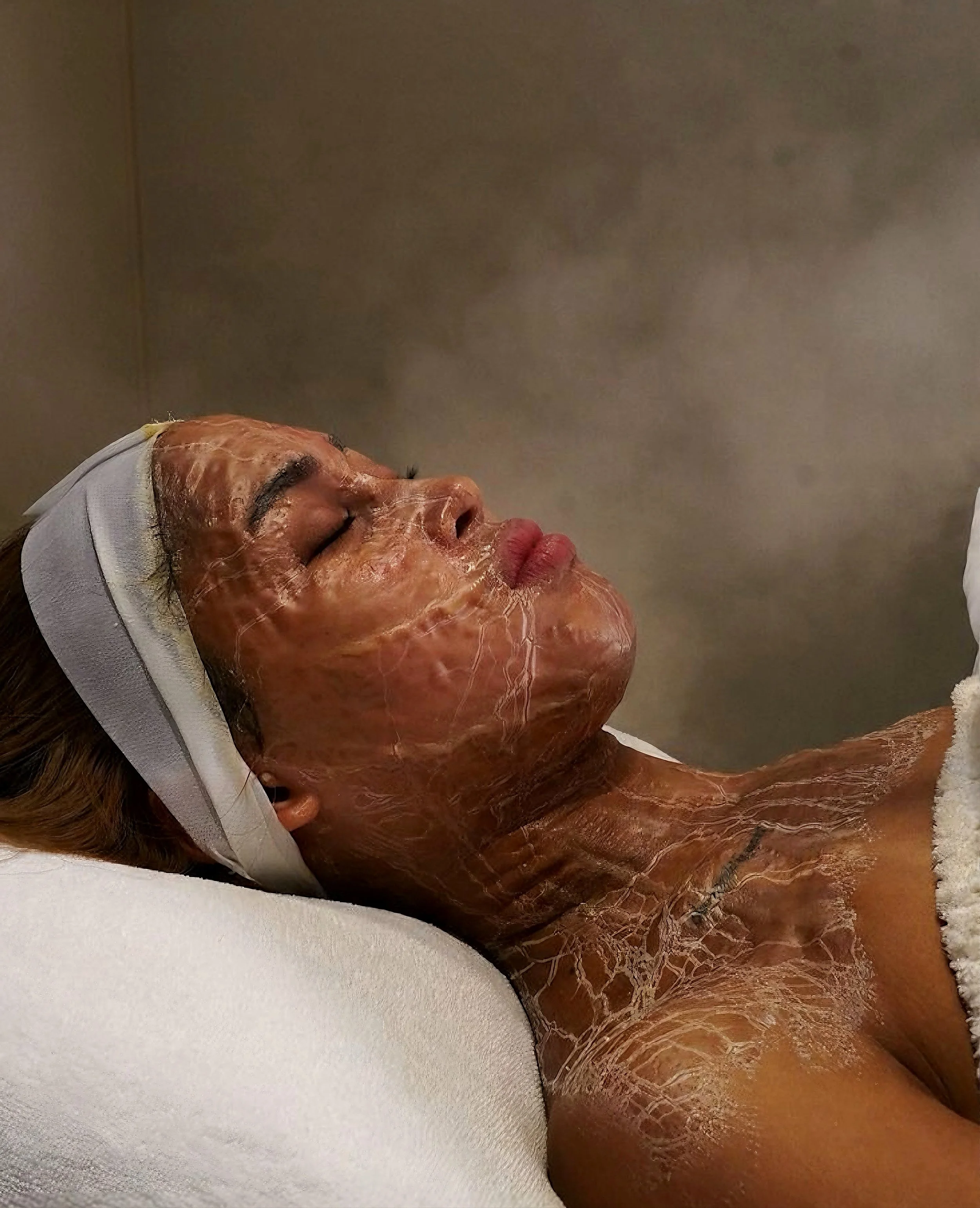 Person lying down with a facial mask, eyes closed, in a spa or skincare treatment setting.