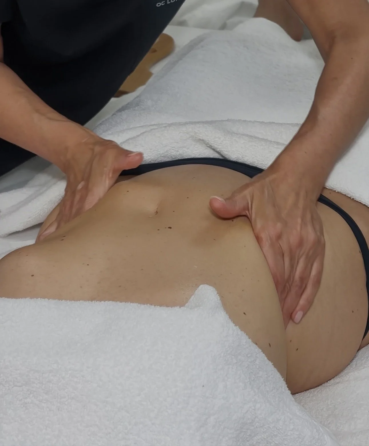A person receiving a massage on their back while lying face down on a white towel.