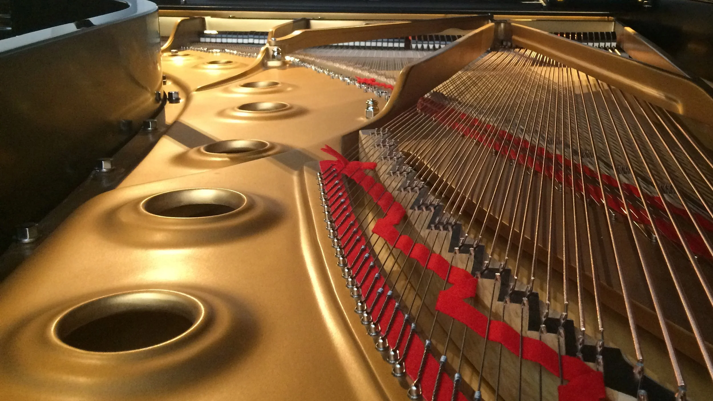 Close-up view of the interior of a grand piano, showing the gold-colored metal frame, strings, and tuning pins.