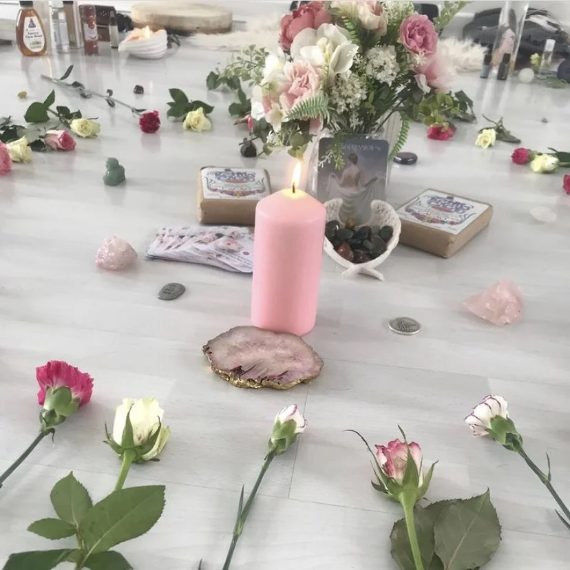 A table decorated with flowers, candles, crystals, and tarot cards, forming a spiritual or ritual setup.