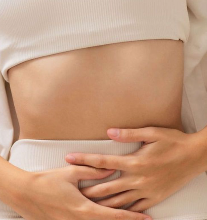 A person holding their stomach with both hands, wearing a white top and pants.