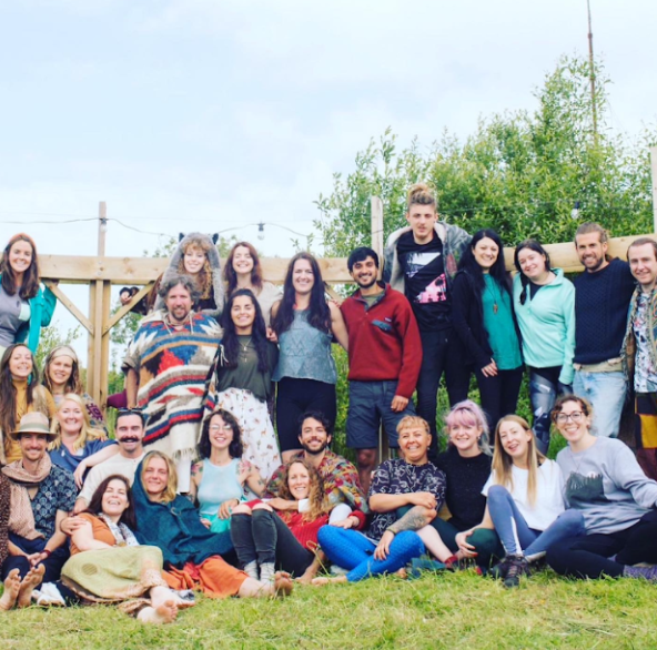 Group of people smiling outdoors in a garden with a wooden structure and trees in the background.