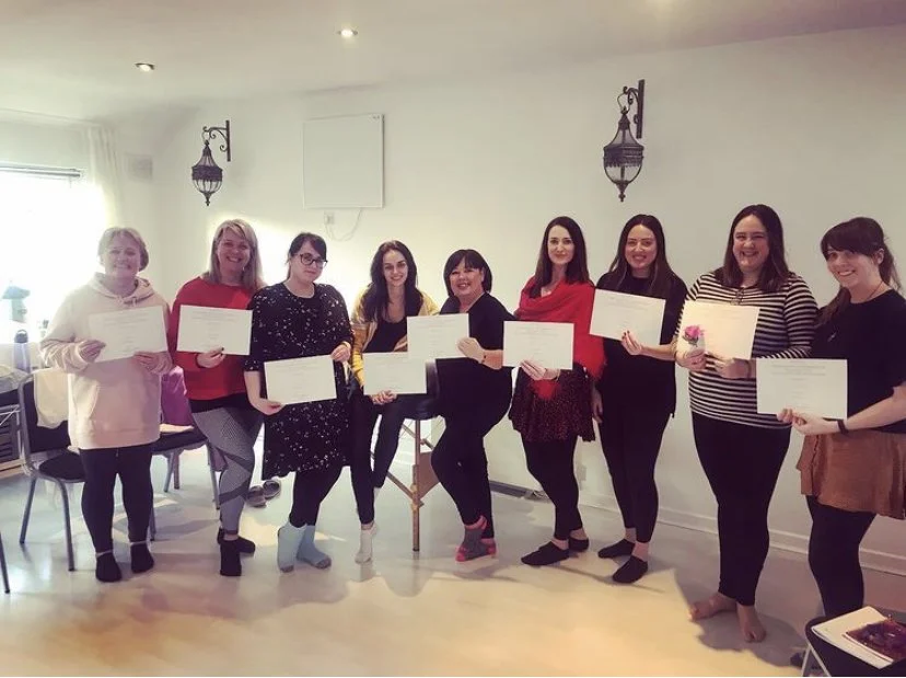 Group of nine women standing indoors, holding certificates, smiling, celebrating achievement.
