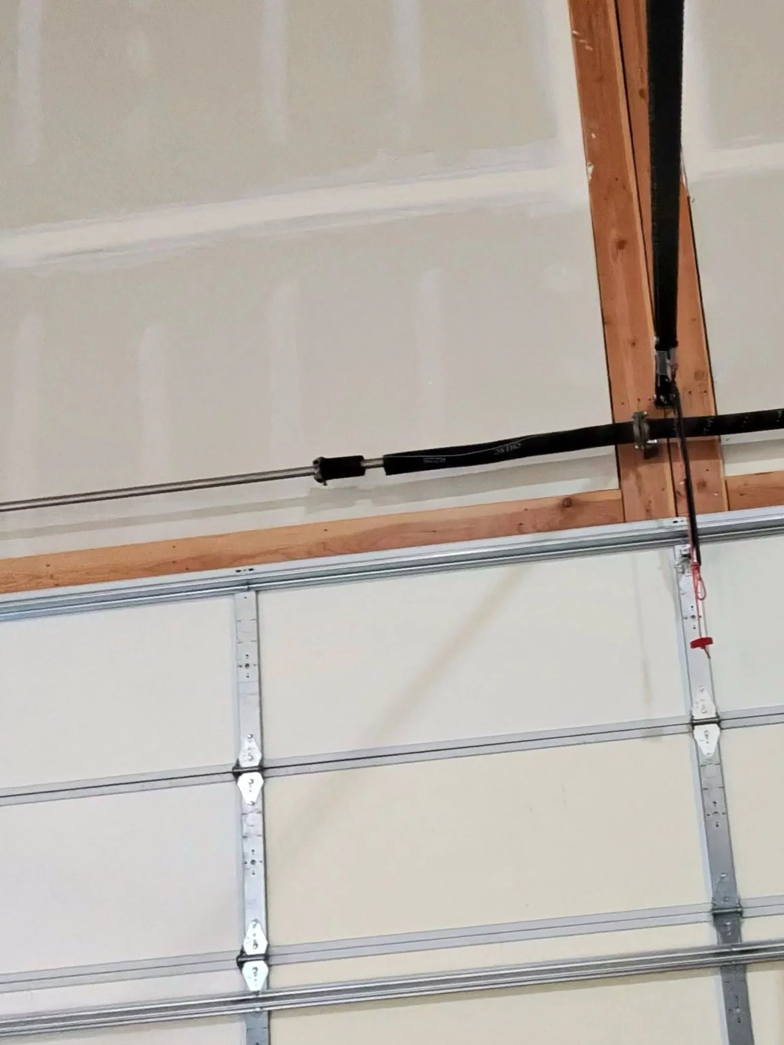 Empty garage door with metal rails and a track system, with electrical wiring and a garage door opener motor.