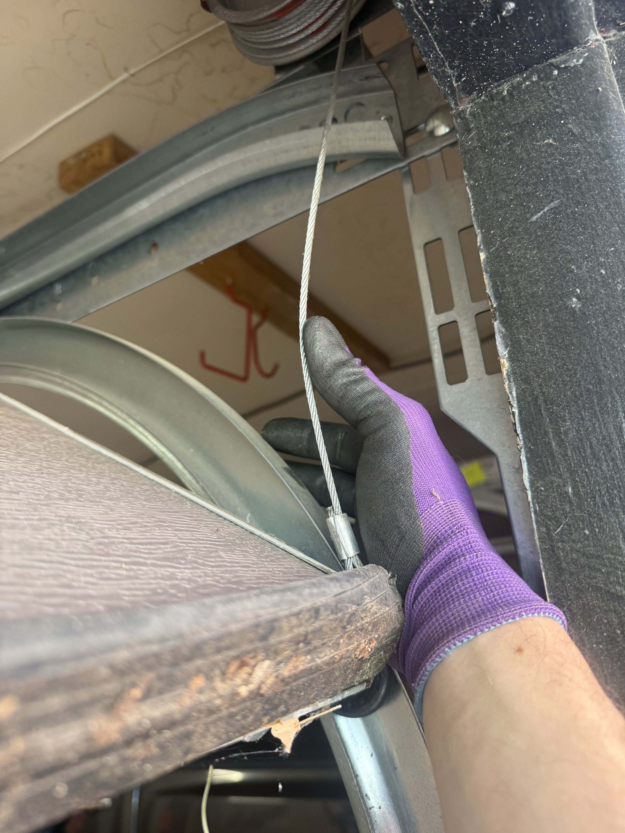 A person wearing a purple glove is holding a metal cable or wire near a metal frame or structure, possibly working on fixing or adjusting it.