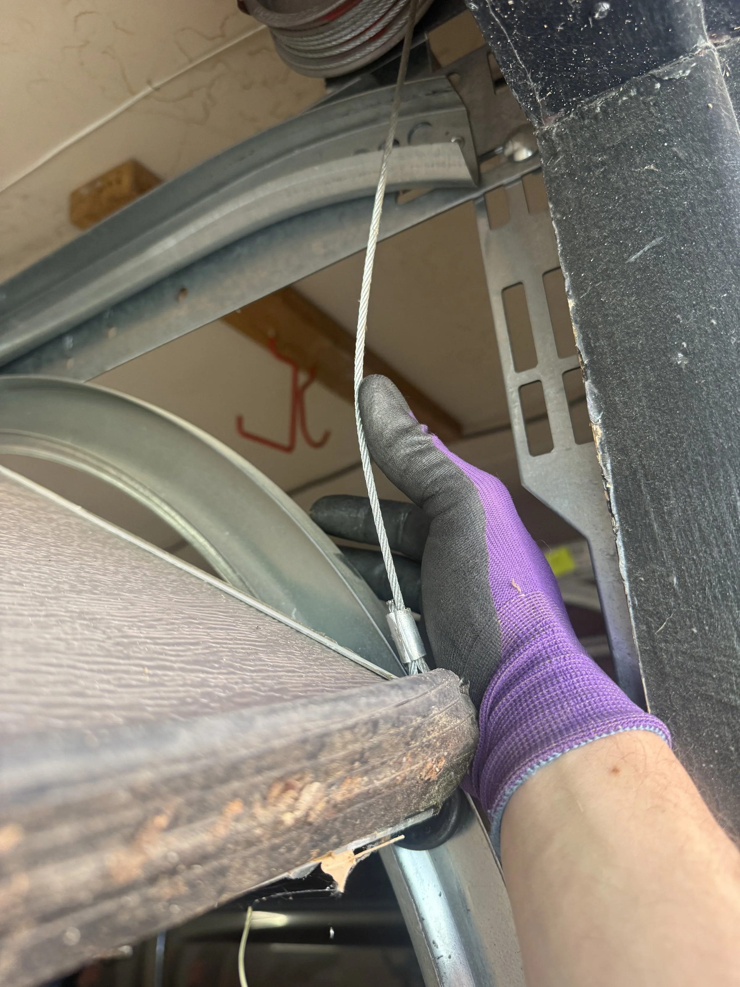 Person wearing purple glove using a wire to repair or cut a metal surface on a garage or workshop setting.
