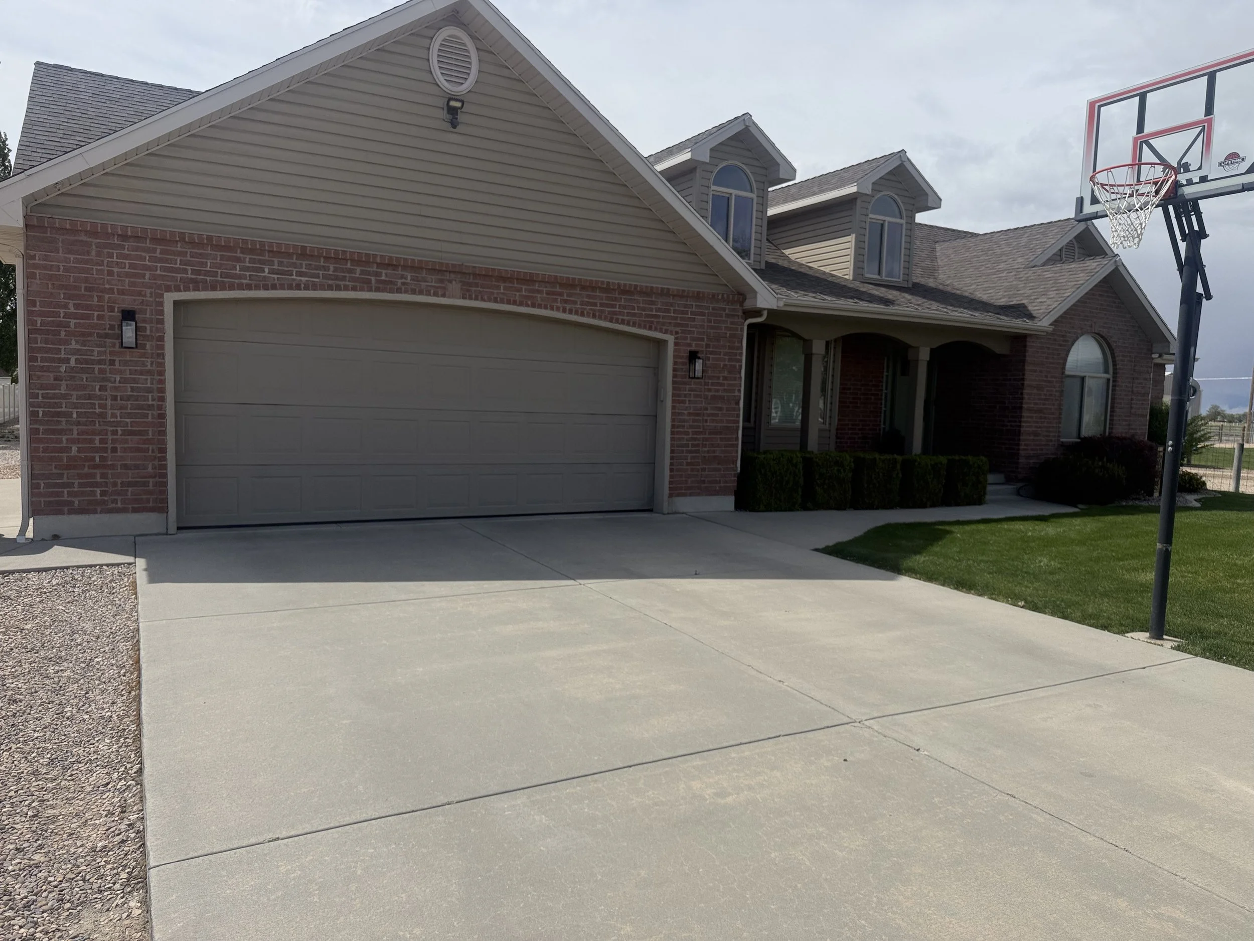 A house with a brick and siding exterior, a garage door, a front yard with grass and a concrete driveway, and a basketball hoop.
