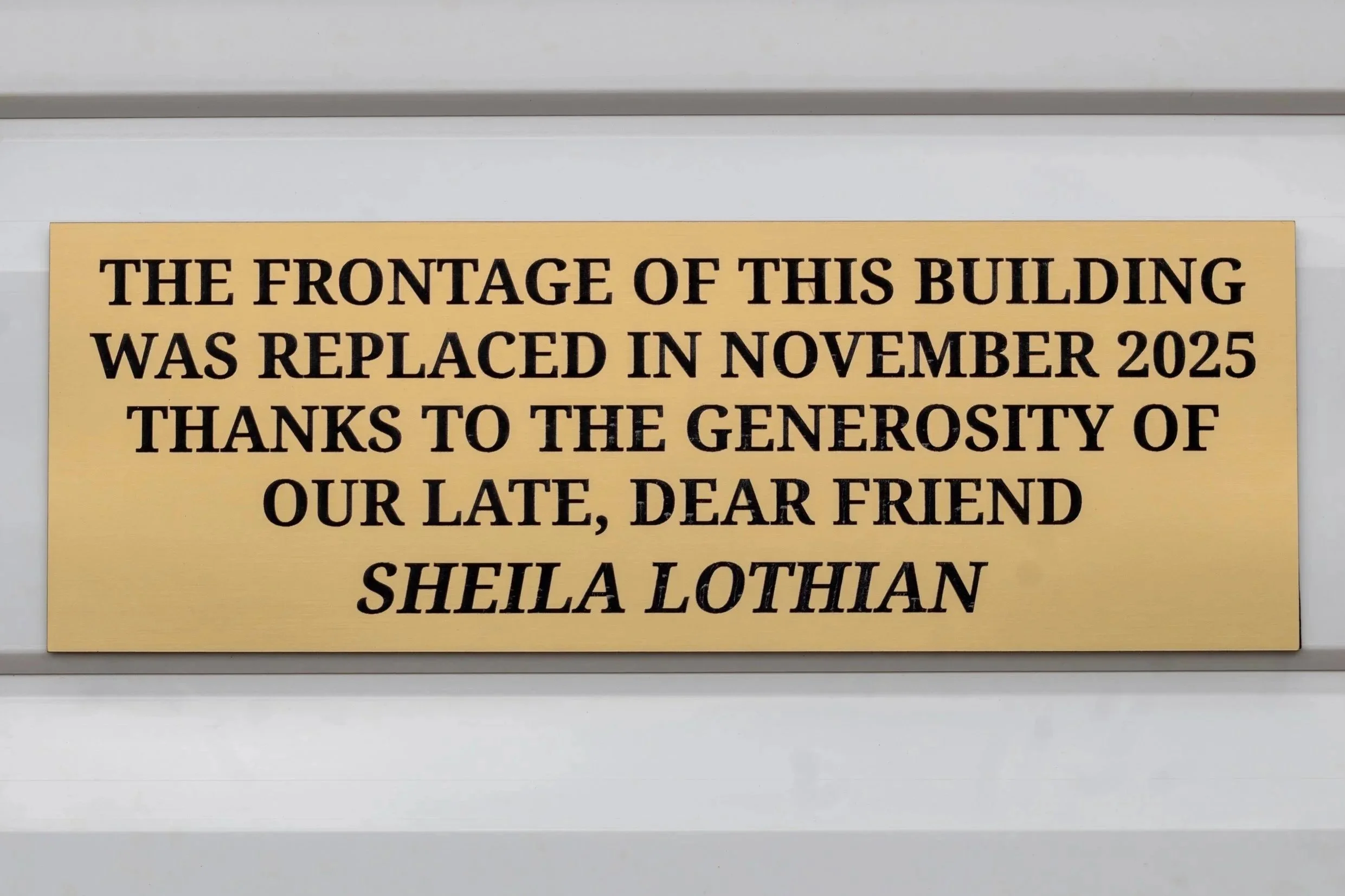 Sheila Lothian plaque outside the Prestwick Howie Building is gold and engraved with black text which reads "the frontage of this building was replaced in November 2025, thanks to the generosity of our late, dear friend Sheila Lothian.