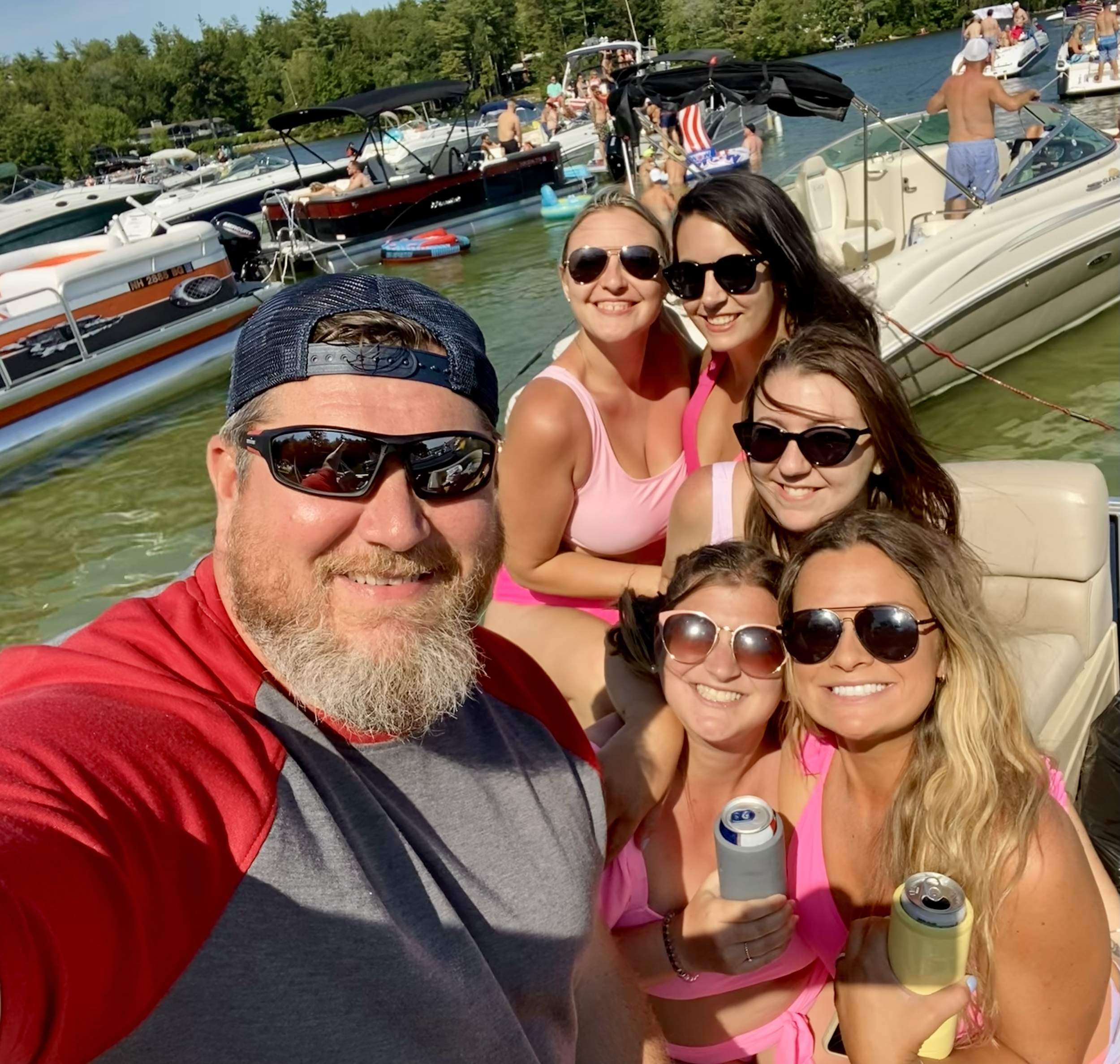 A group of people on boats and swimming equipment enjoying a day on the water, with some people taking a selfie and wearing sunglasses.