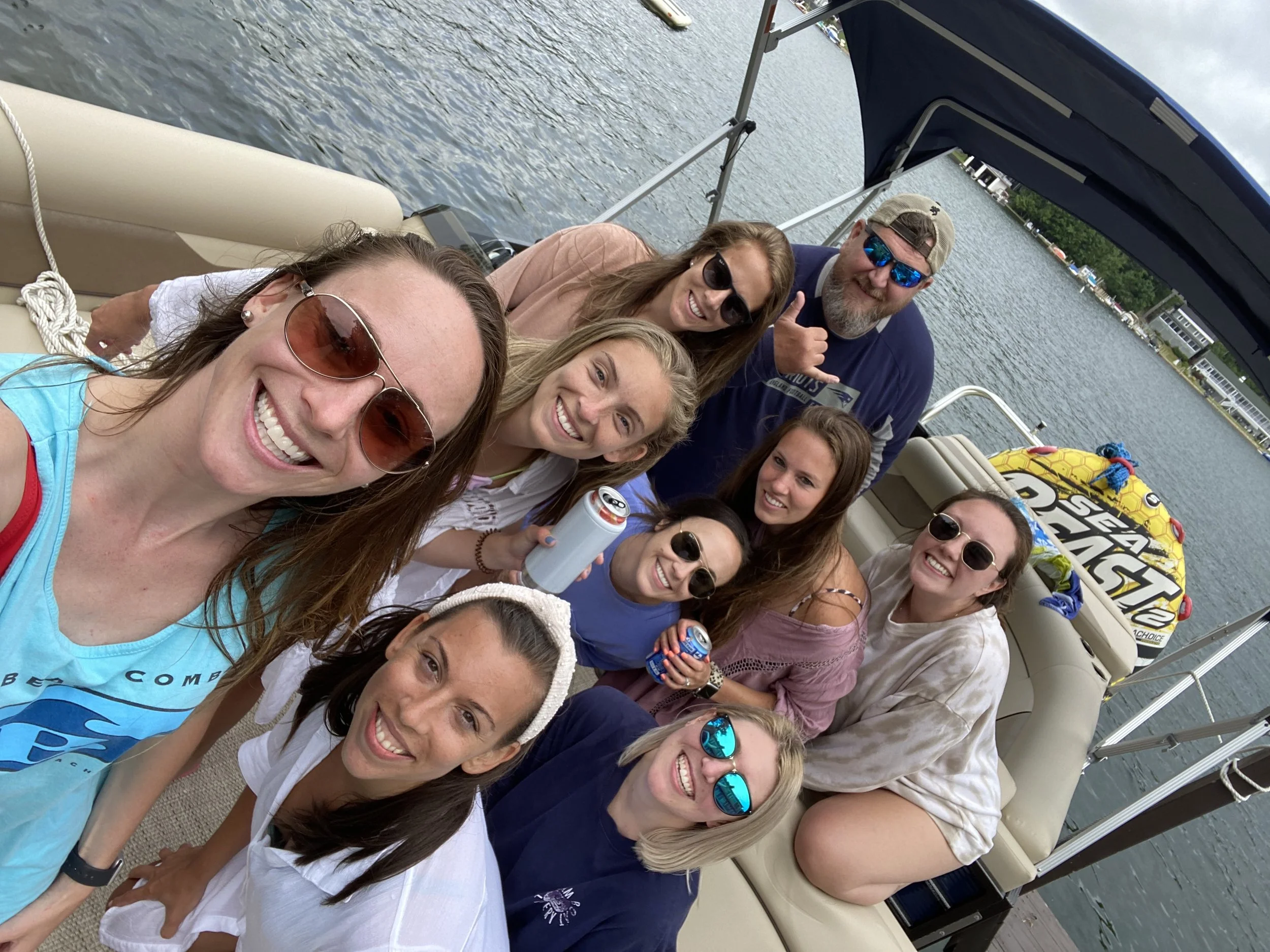 A group of friends on a boat smiling and enjoying a day on the water, with some wearing sunglasses and holding drinks.