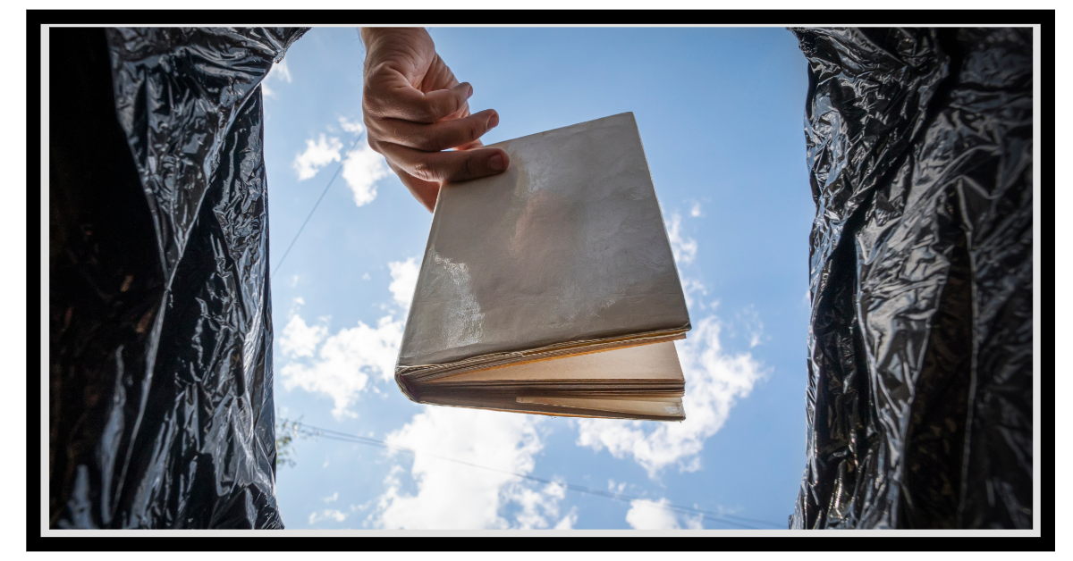 Image of book being thrown away from the view of the bottom of the trash bag