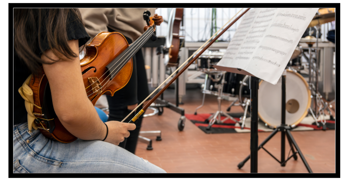 image of student with violin and bow in what looks like a band room