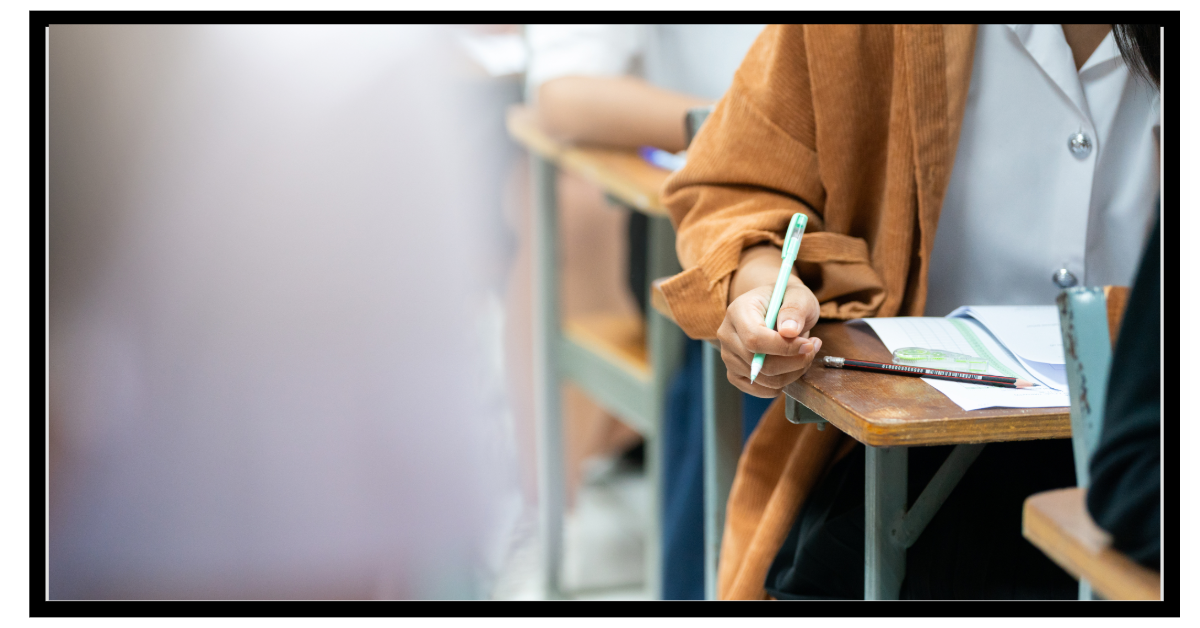 someone sitting in a row of desks working with pen and pencil