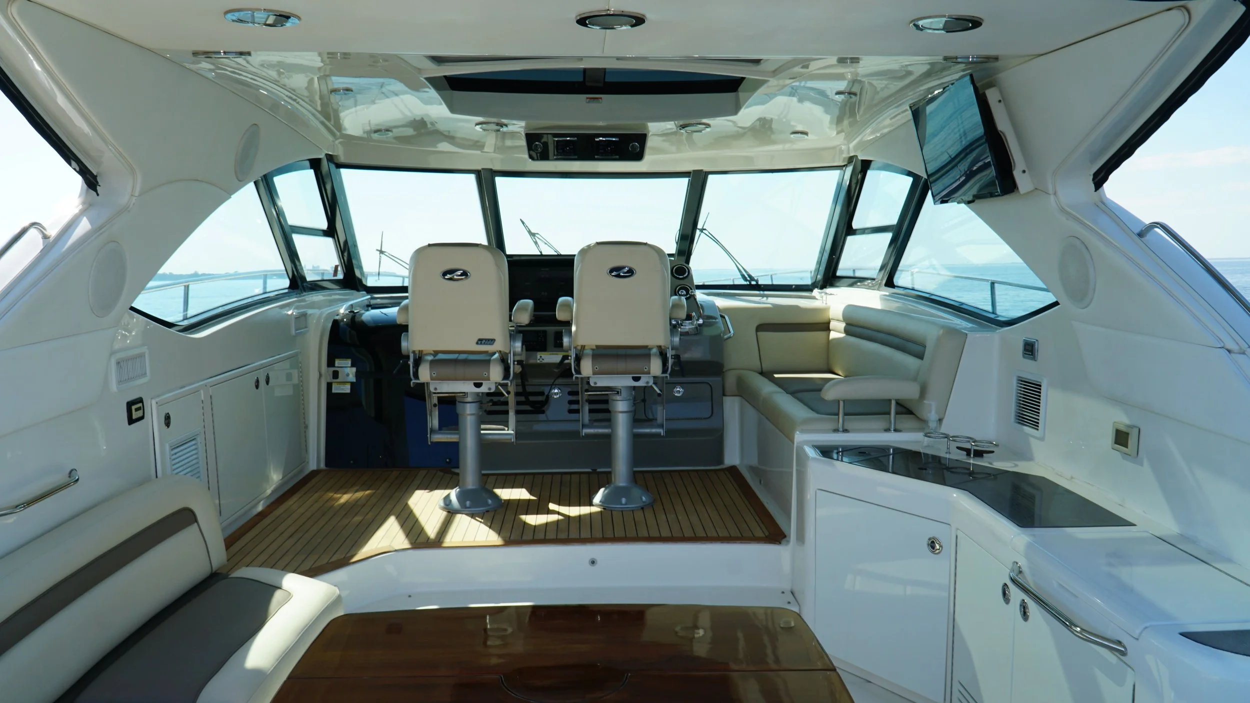Interior of a yacht's bridge with captain and crew seats, a flat-screen TV, windows showing water and sky, and navigation equipment. Lessons available for electronics.