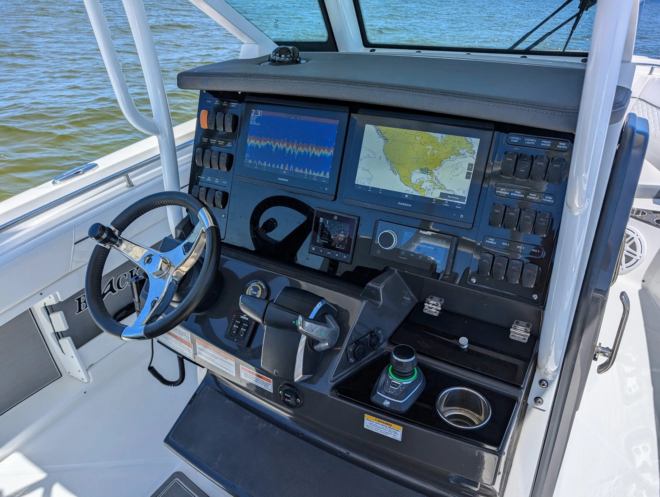 Close-up of a boat's navigation and control dashboard with multiple screens and gauges, surrounded by water. Yamaha helm master controls during boat lessons.