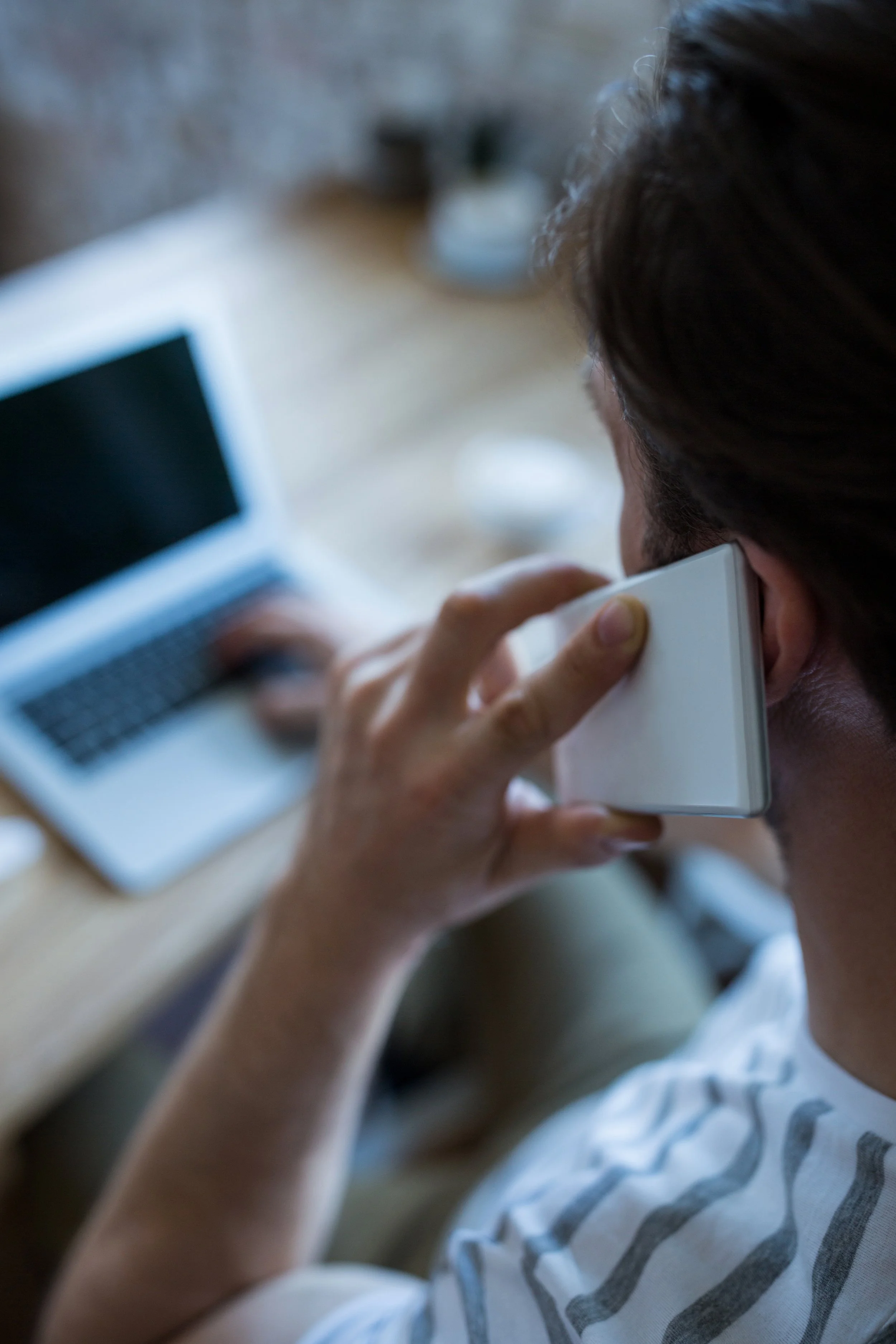A person talking on a landline phone while sitting at a desk with a laptop.