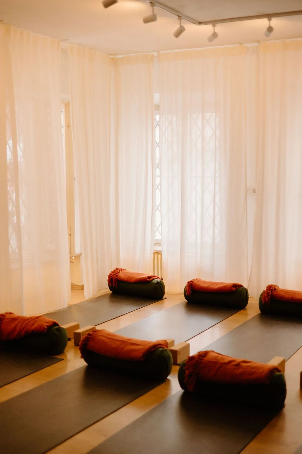 Yoga mats with bolsters and blankets arranged in a room with sheer curtains