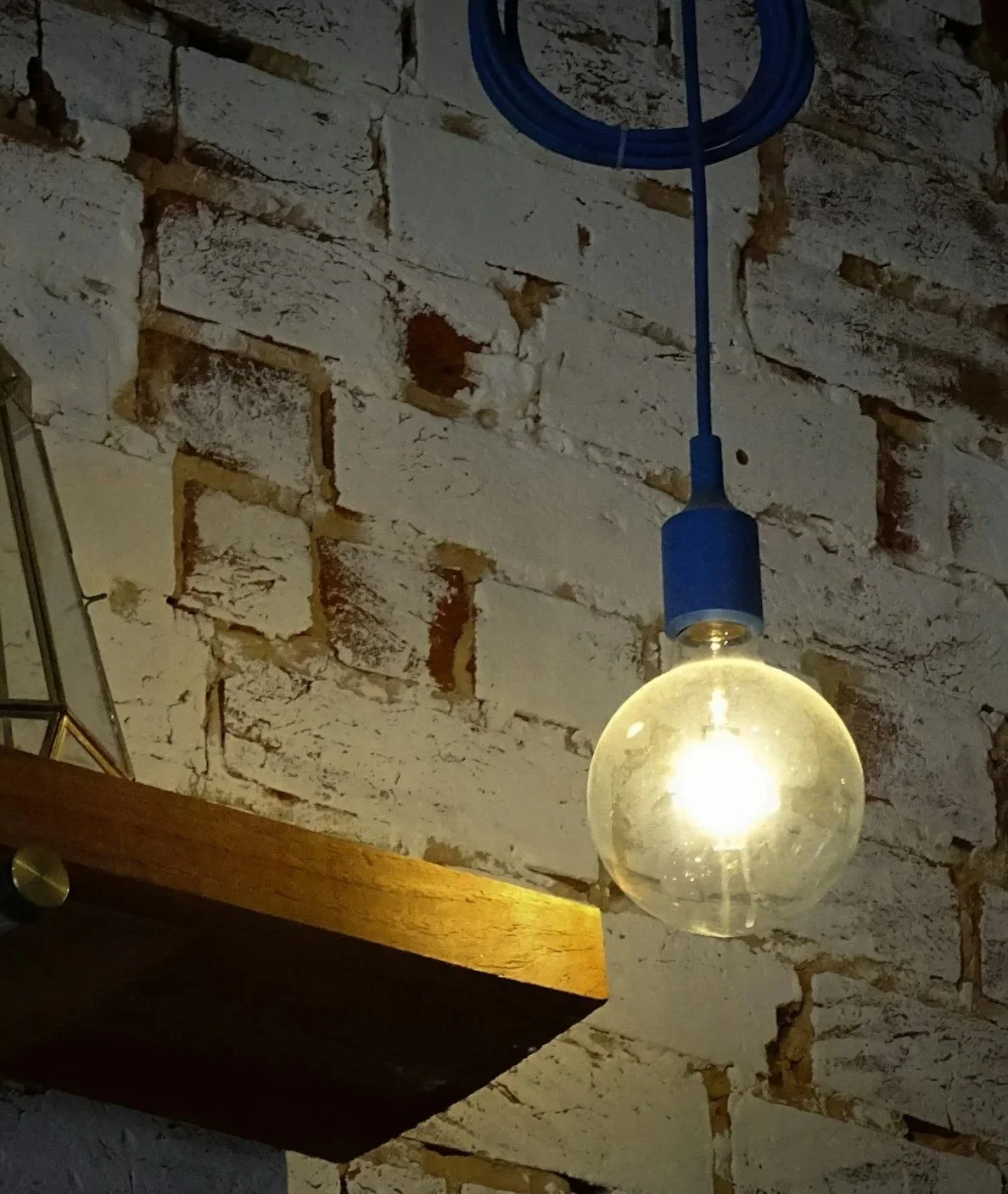 A glowing light bulb hanging from a blue cord against a white brick wall.