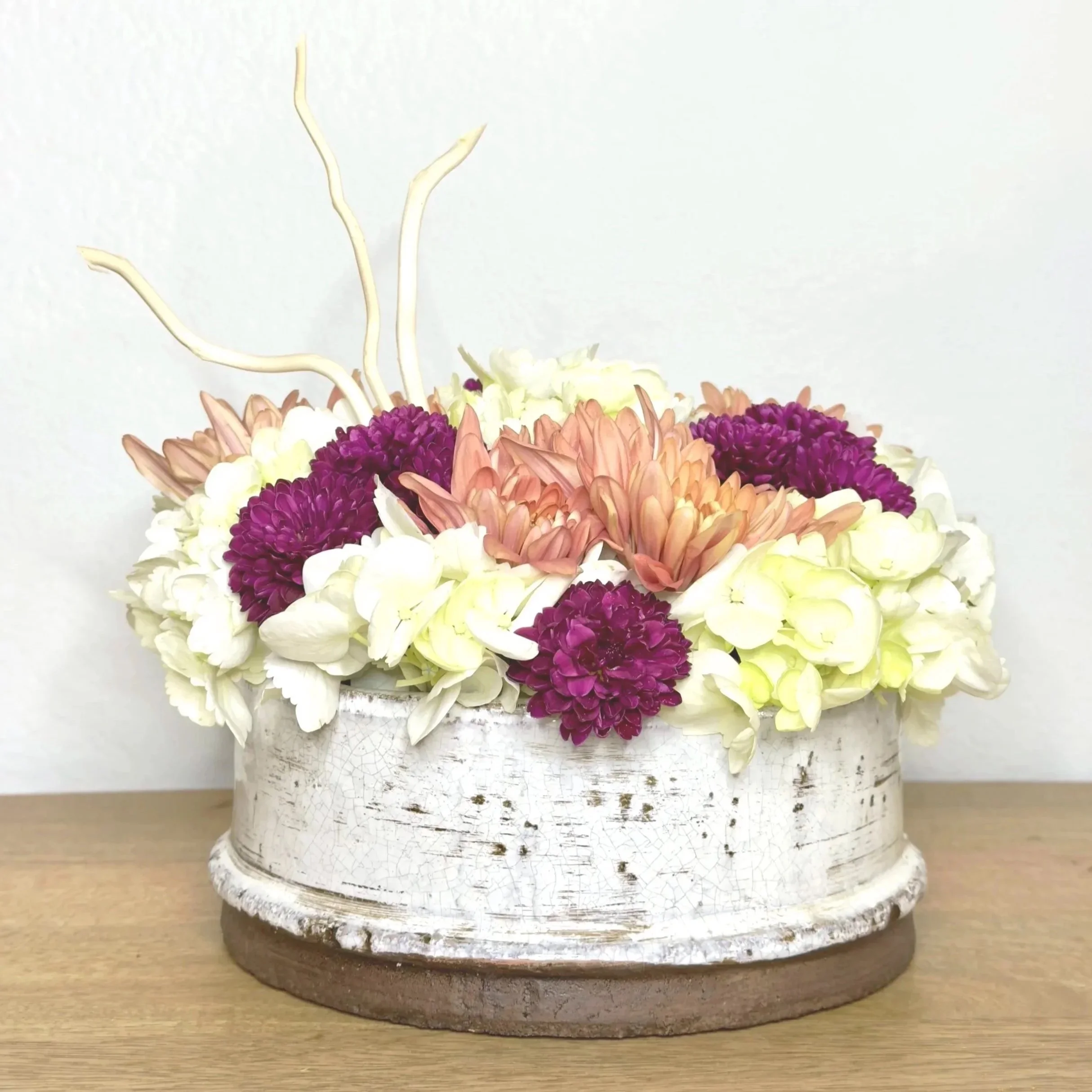 A floral arrangement in a vintage, crackled white ceramic vase on a wooden surface.