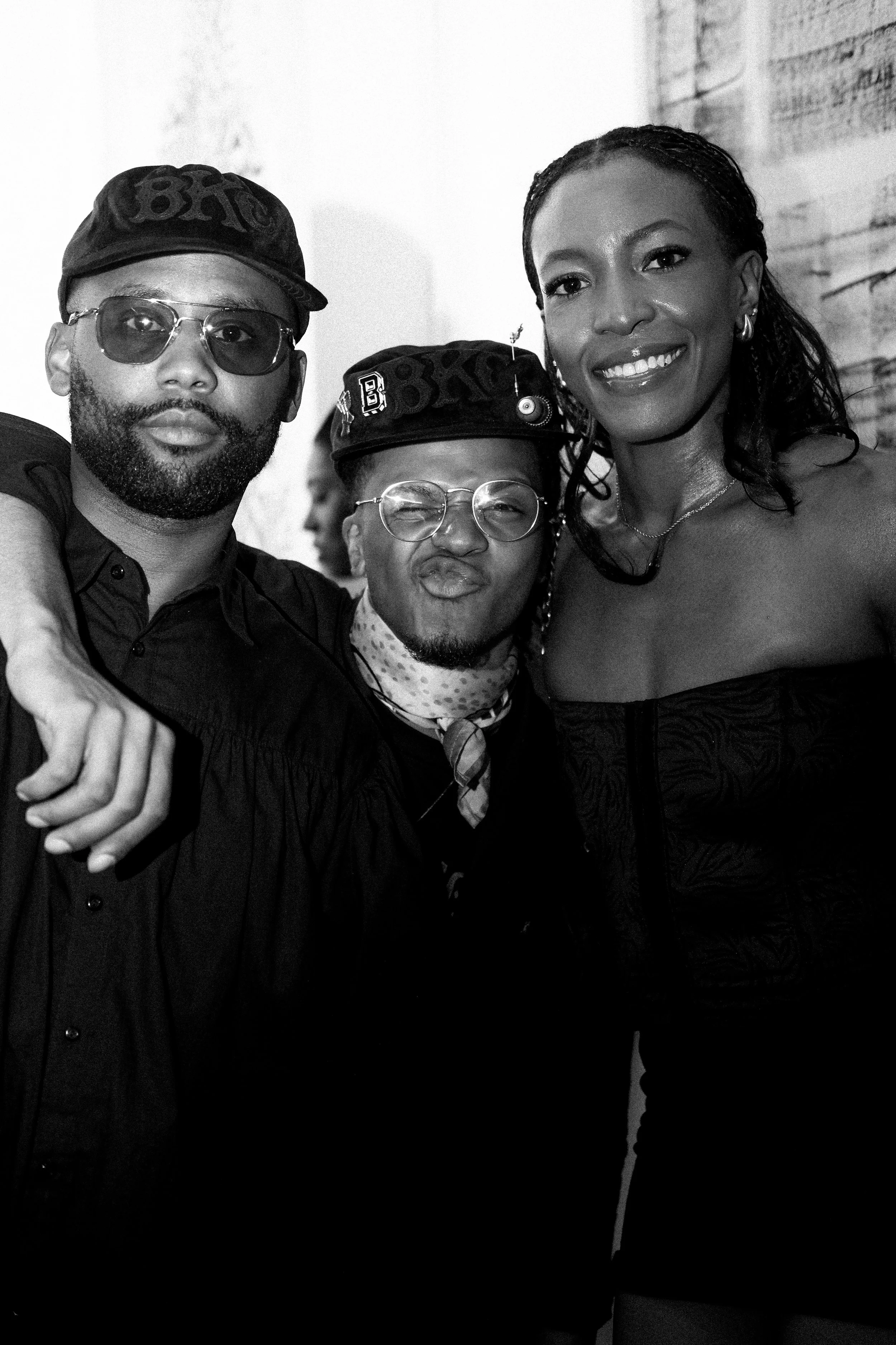 Three people posing together at a social event, smiling and dressed in fashionable clothing, with one woman and two men.