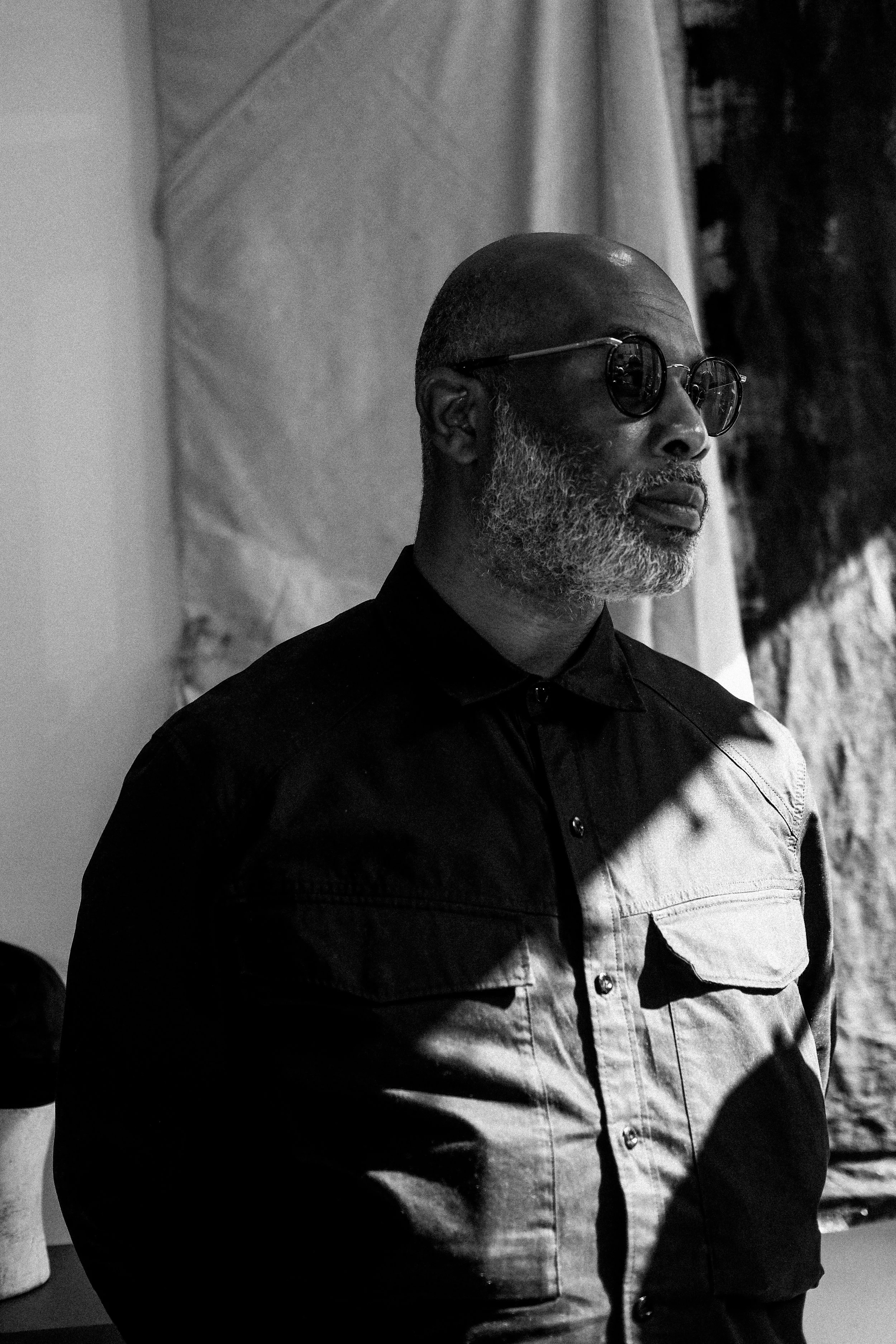 Portrait of a middle-aged man with a beard and glasses, wearing a half-light and half-dark shirt, in a black-and-white photo.
