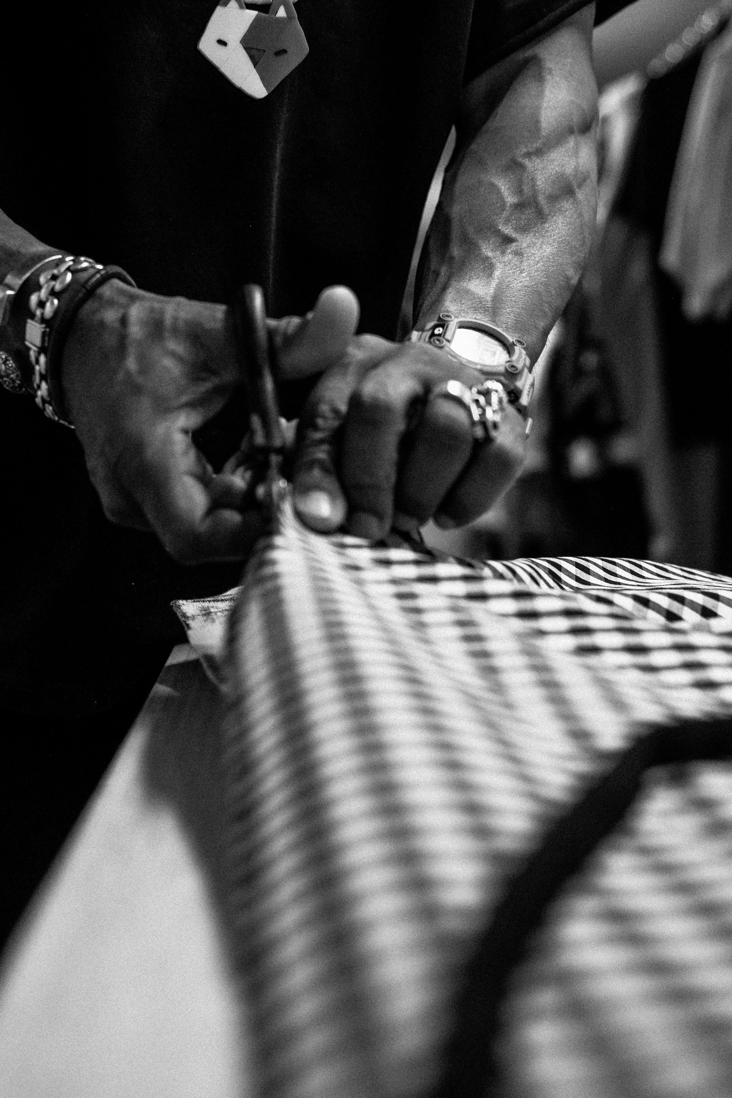 Person working on a fabric with scissors, wearing Rings, a watch, and a bracelet in black and white.