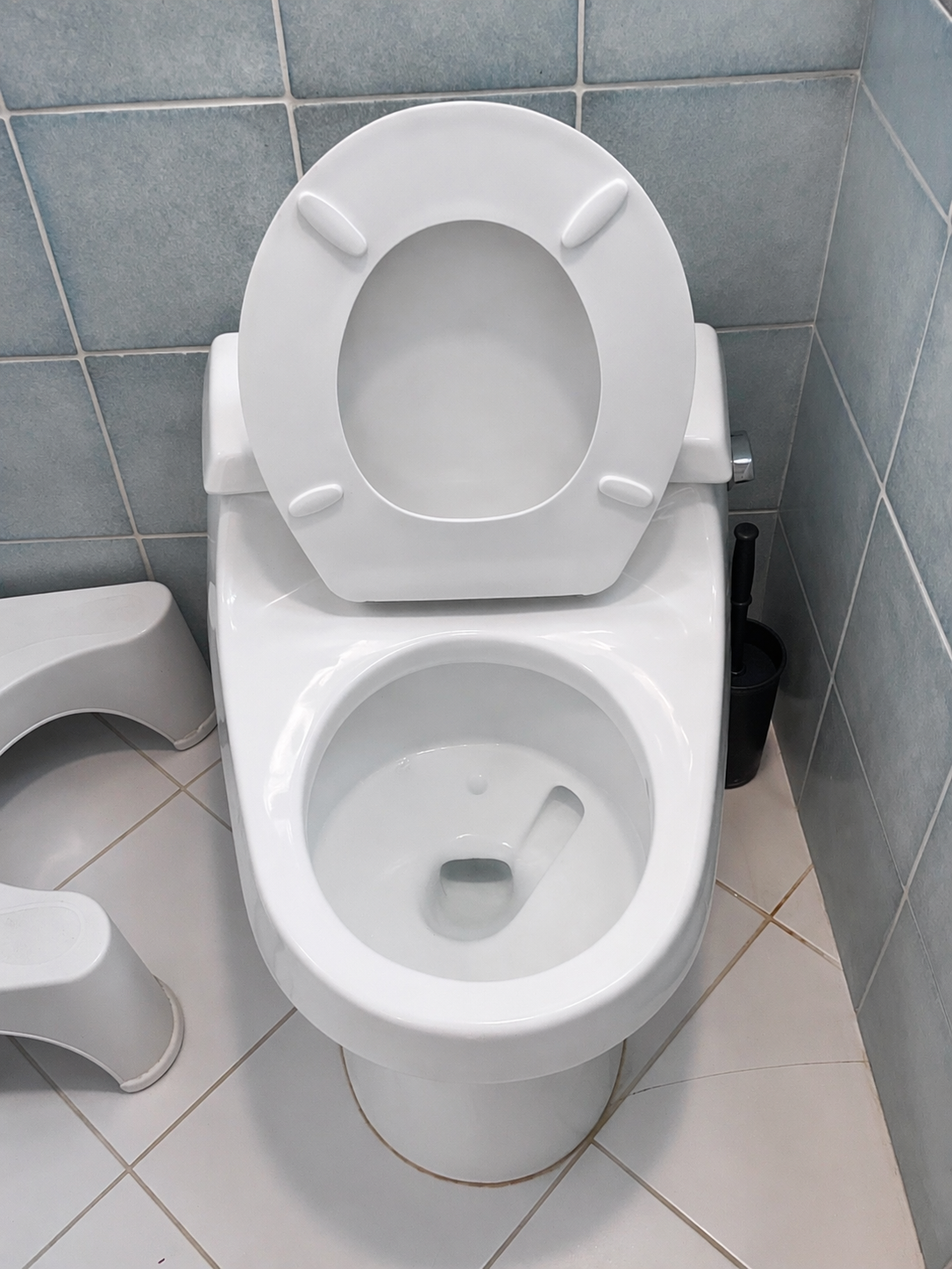 A white modern toilet in a tiled bathroom with the toilet seat lid open.