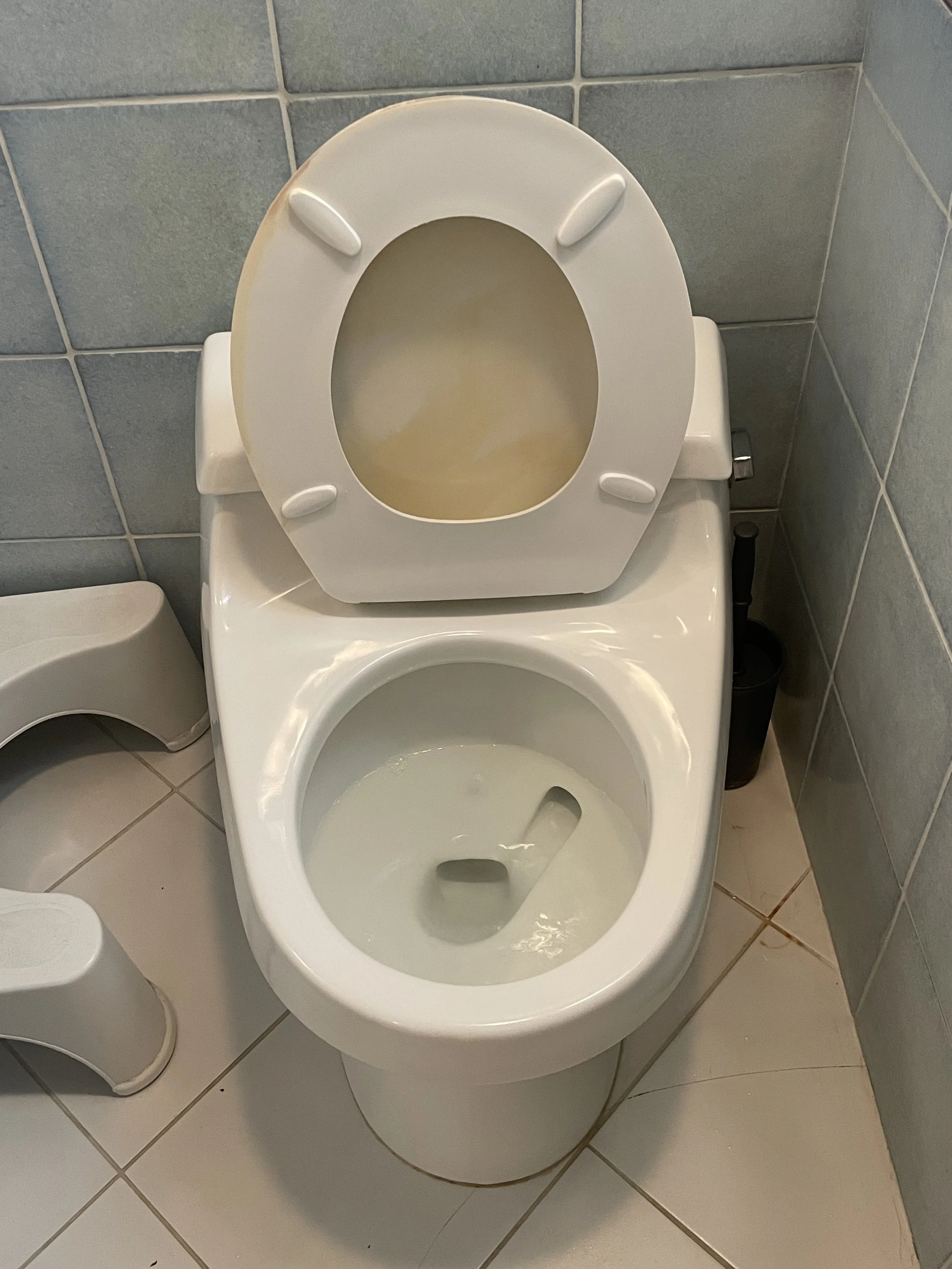 Toilet with the seat up in a bathroom with blue tile walls and white tiled floor