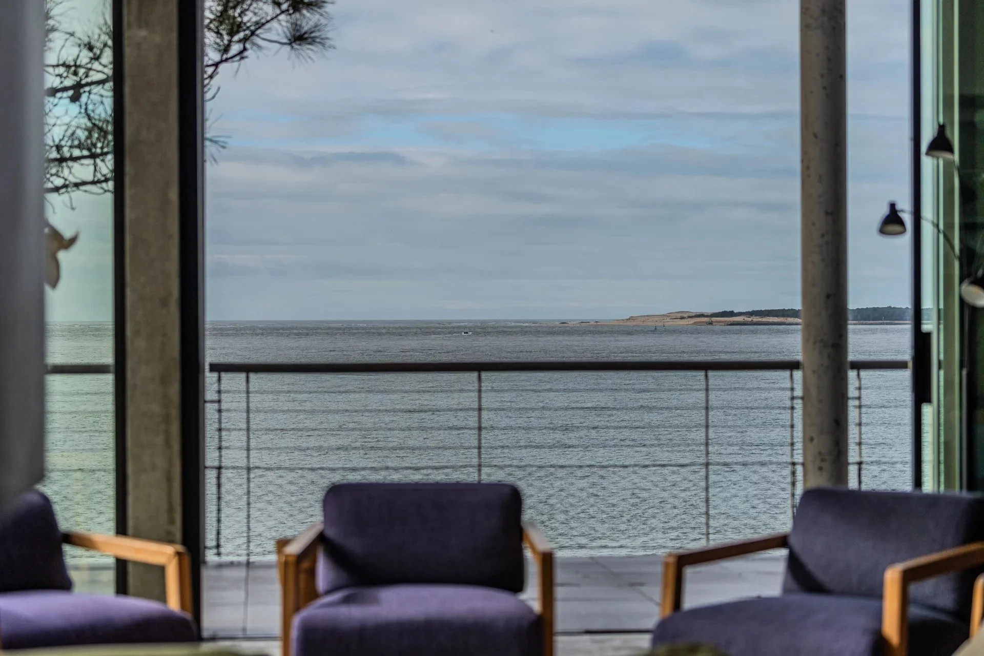 Vue panoramique sur la mer depuis un balcon avec fauteuils et grandes fenêtres