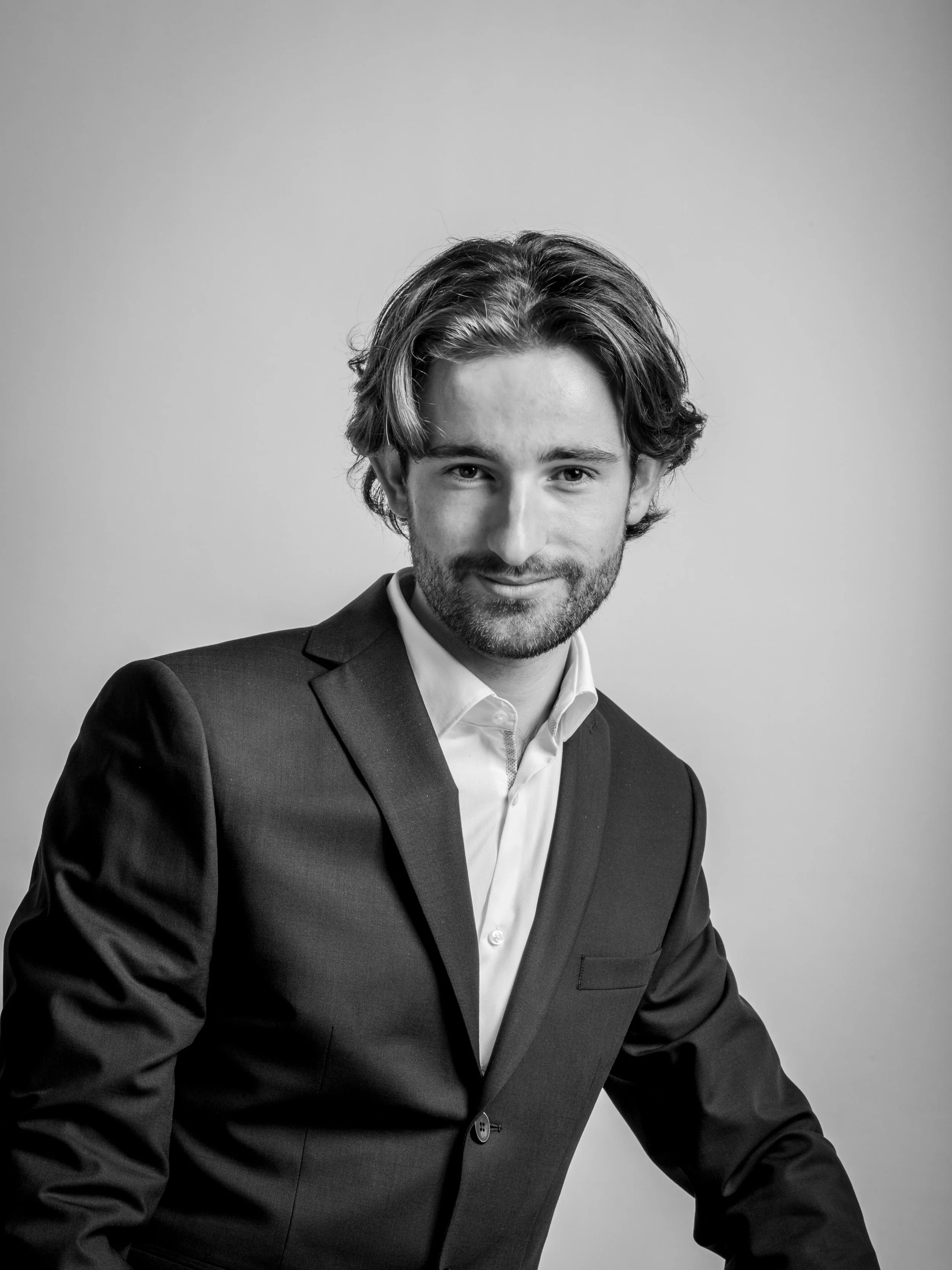 jeune homme souriant avec cheveux bouclés, portant un costume et une chemise blanche, en noir et blanc
