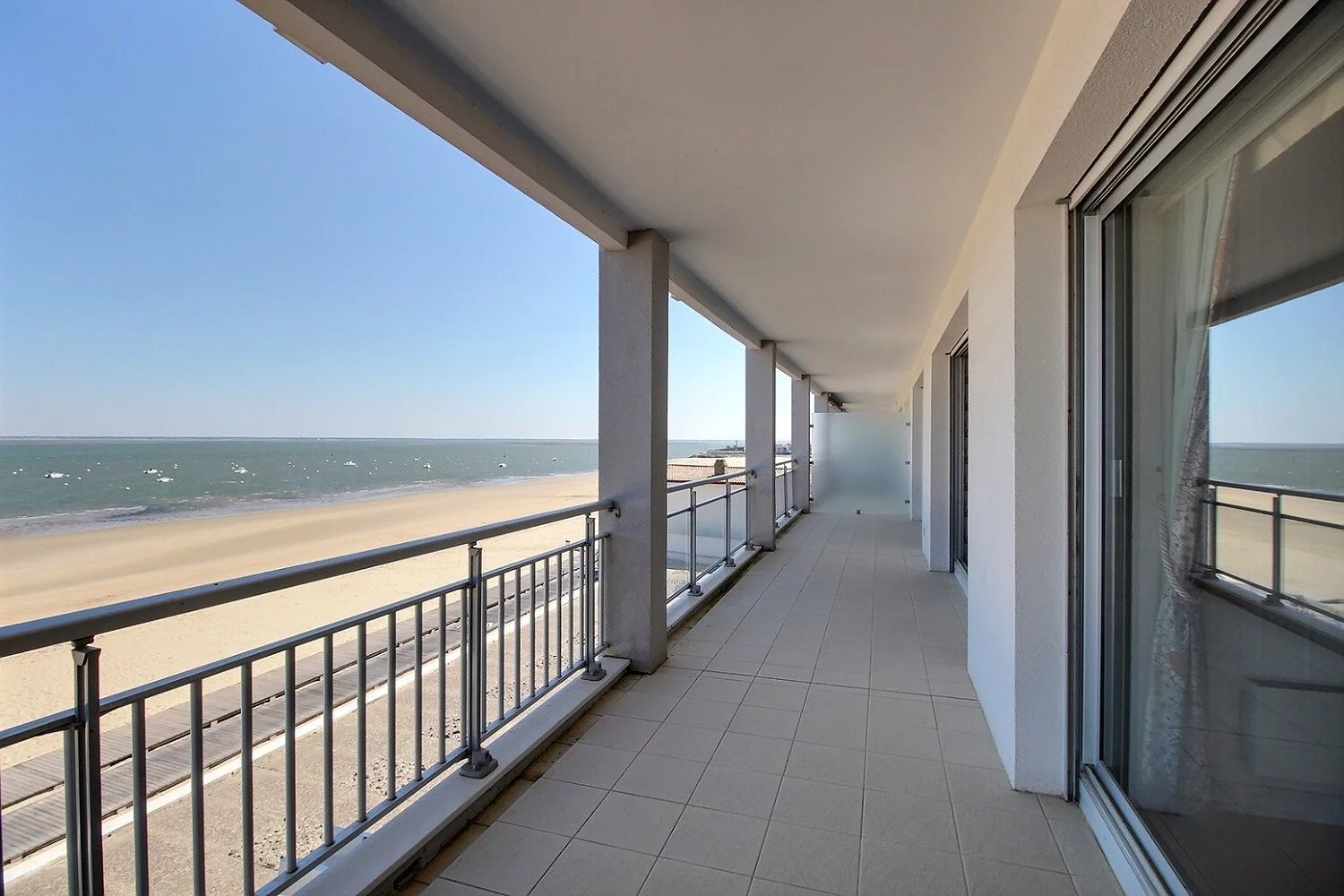 Balcon avec vue sur la mer, plage de sable, ciel clair, with glass doors.