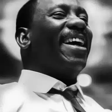 Black-and-white portrait of jazz guitarist and composer Wes Montgomery smiling broadly in a white shirt and dark tie.
